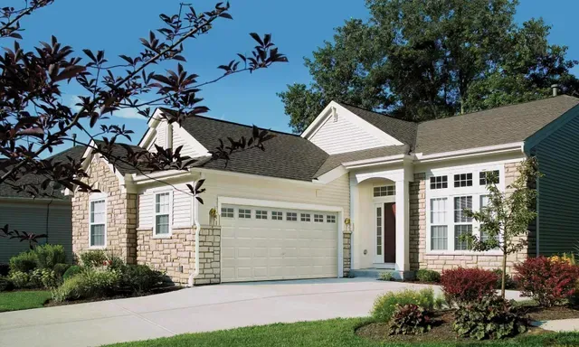 Beige house with a garage and driveway, brick accents, and landscaping.