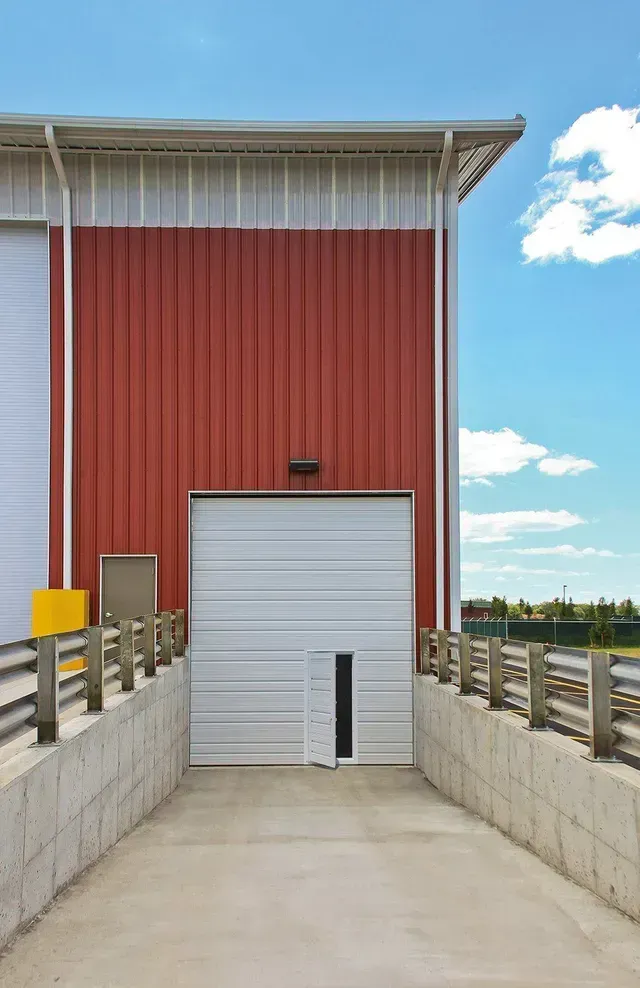 Red and white industrial building with a loading dock and roll-up door against a blue sky.