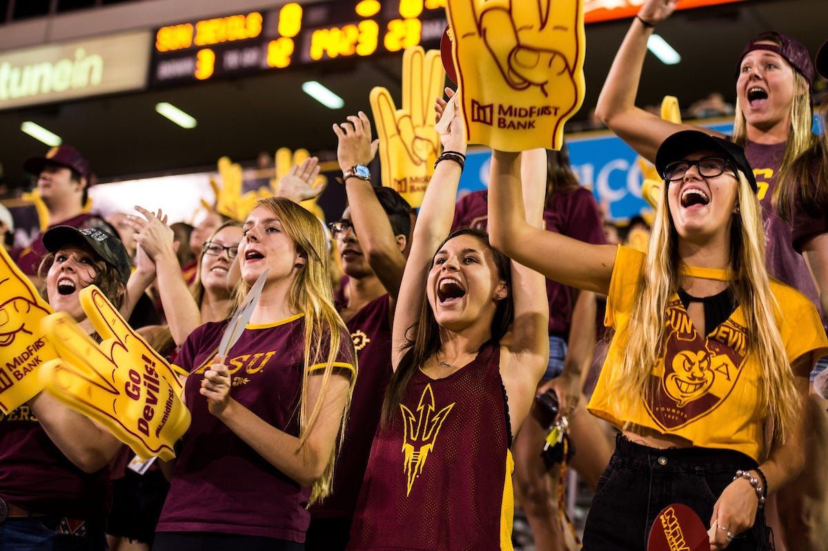 A group of people are standing in a stadium holding up foam fingers.