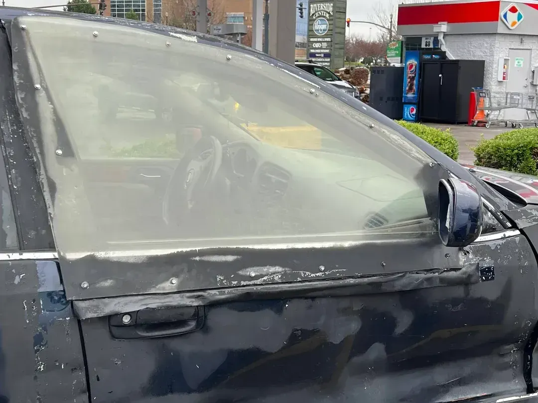 A black car with a broken windshield is parked in front of a gas station.