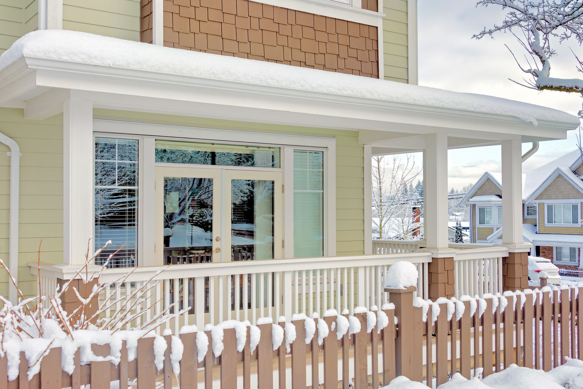 Snow-covered house with a porch and picket fence. Light green siding, white trim, and brown accents.