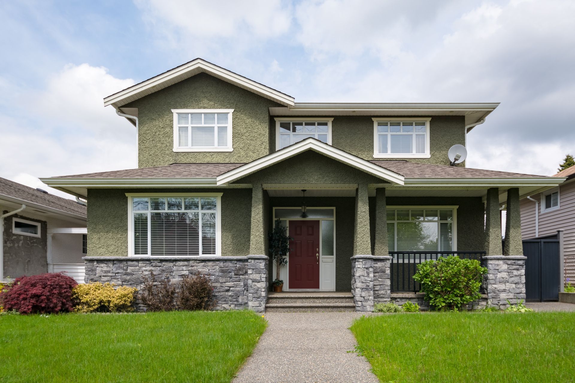 Two-story green house with gray stone accents, a red door, and a concrete path leading to it.