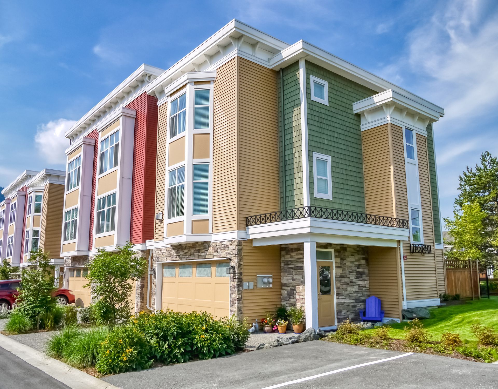 Multi-colored townhouses with a garage, stone accents, and a blue sky.