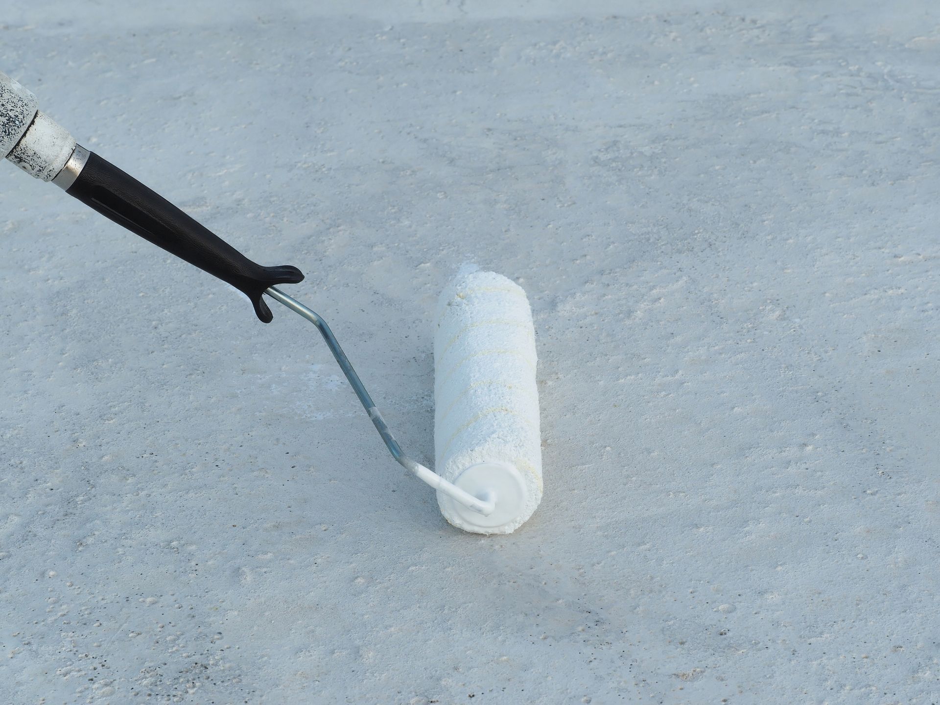 A paint roller applying white coating to a gray surface.