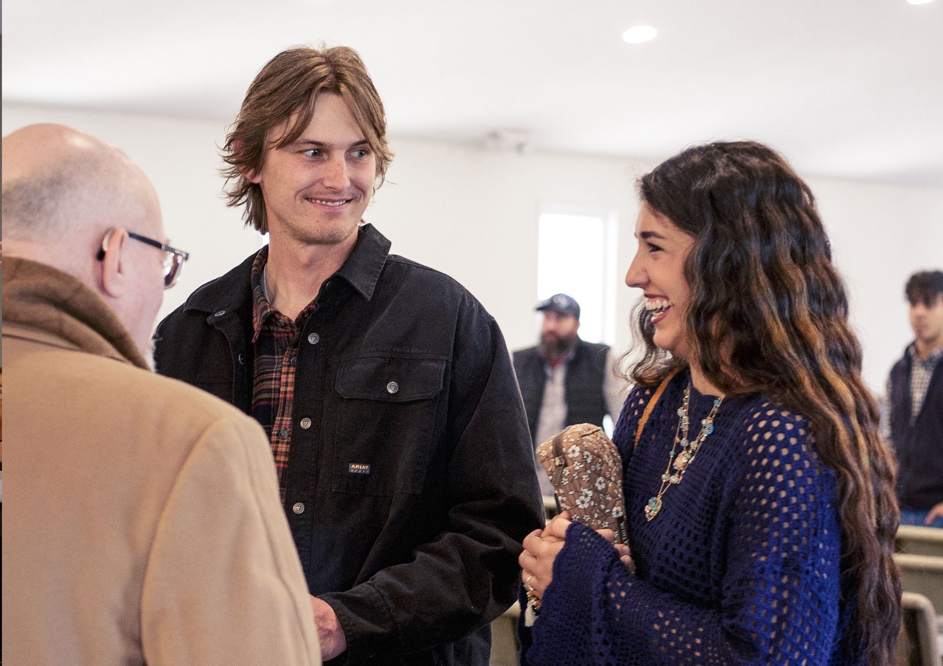 Two men are standing next to each other in a hallway holding books.