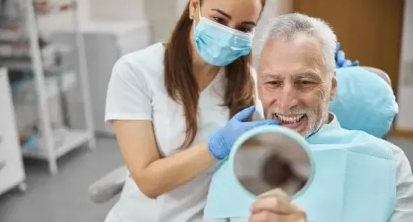A dentist is looking at a patient 's teeth in a mirror.