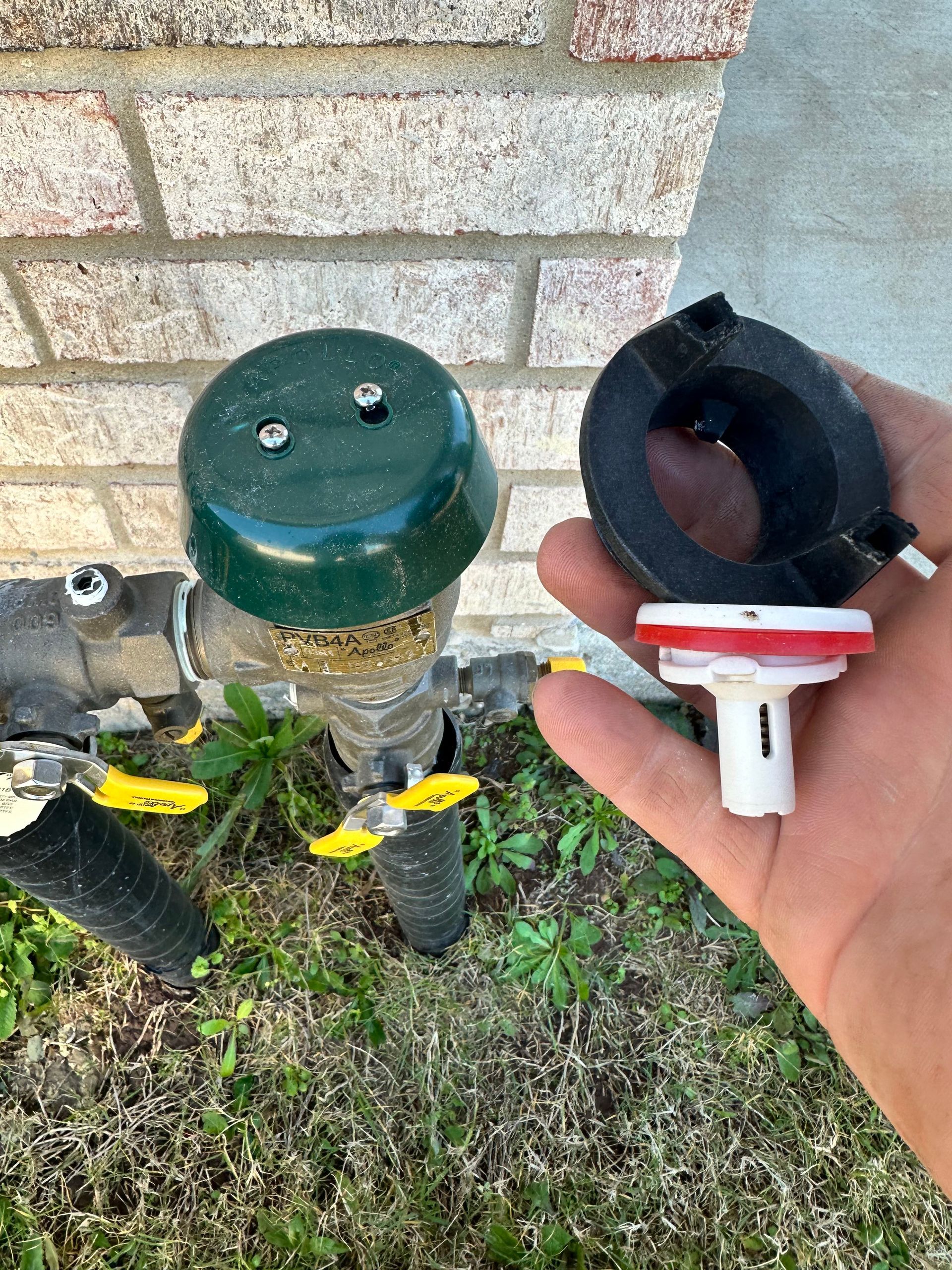 A person is holding a gas valve next to a brick wall.