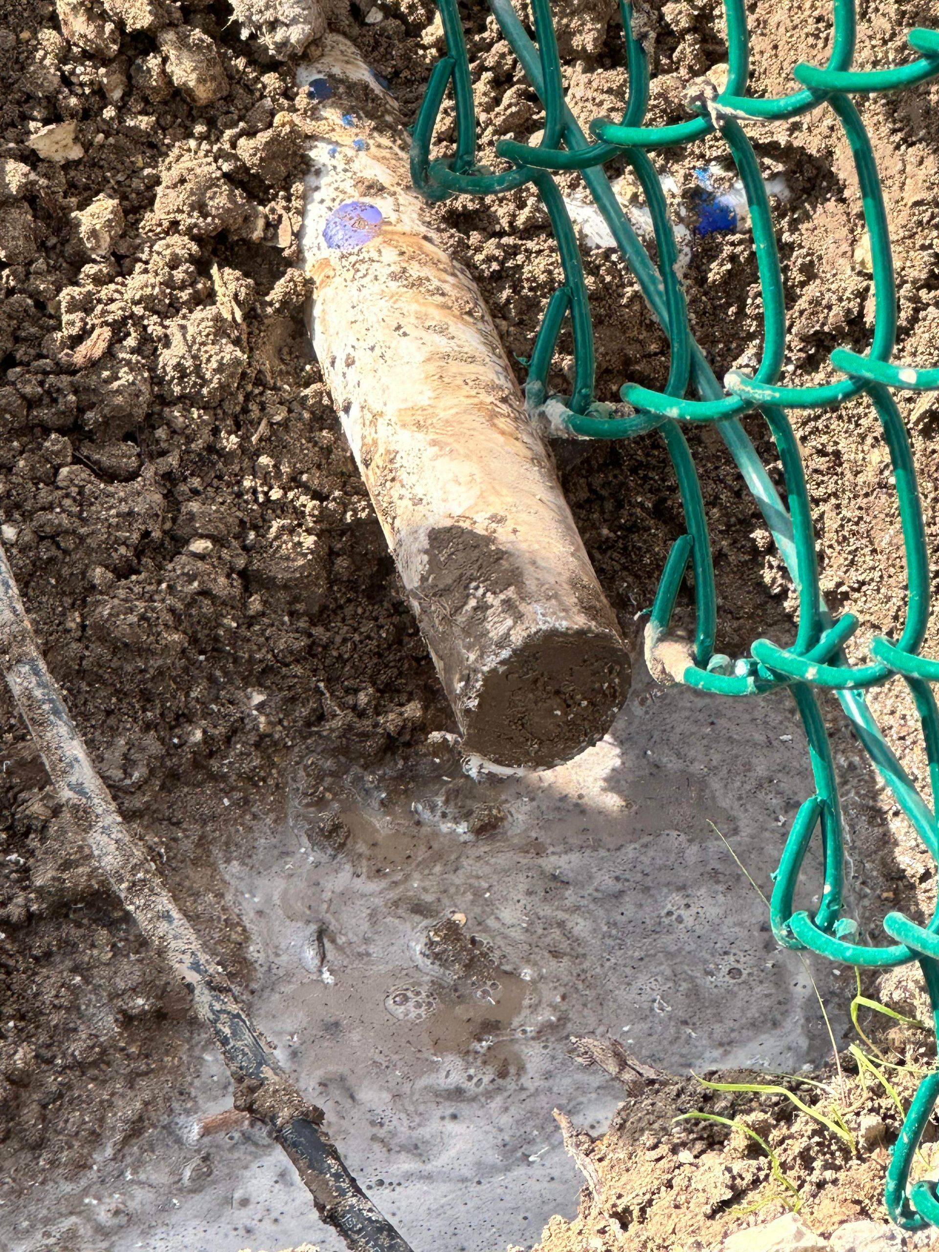 A bottle is sitting in the dirt next to a chain link fence.