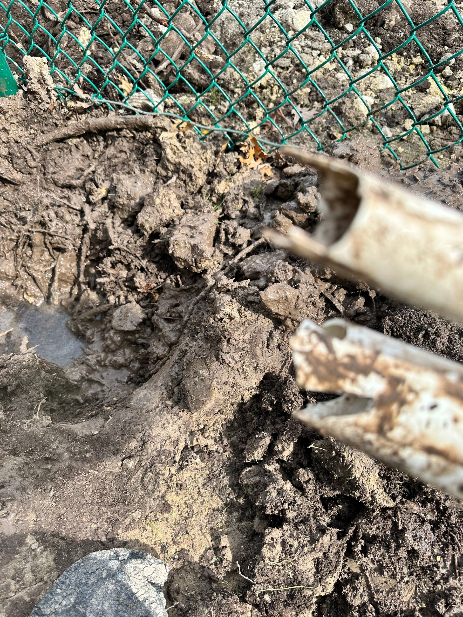 A close up of a shovel in the dirt next to a chain link fence.