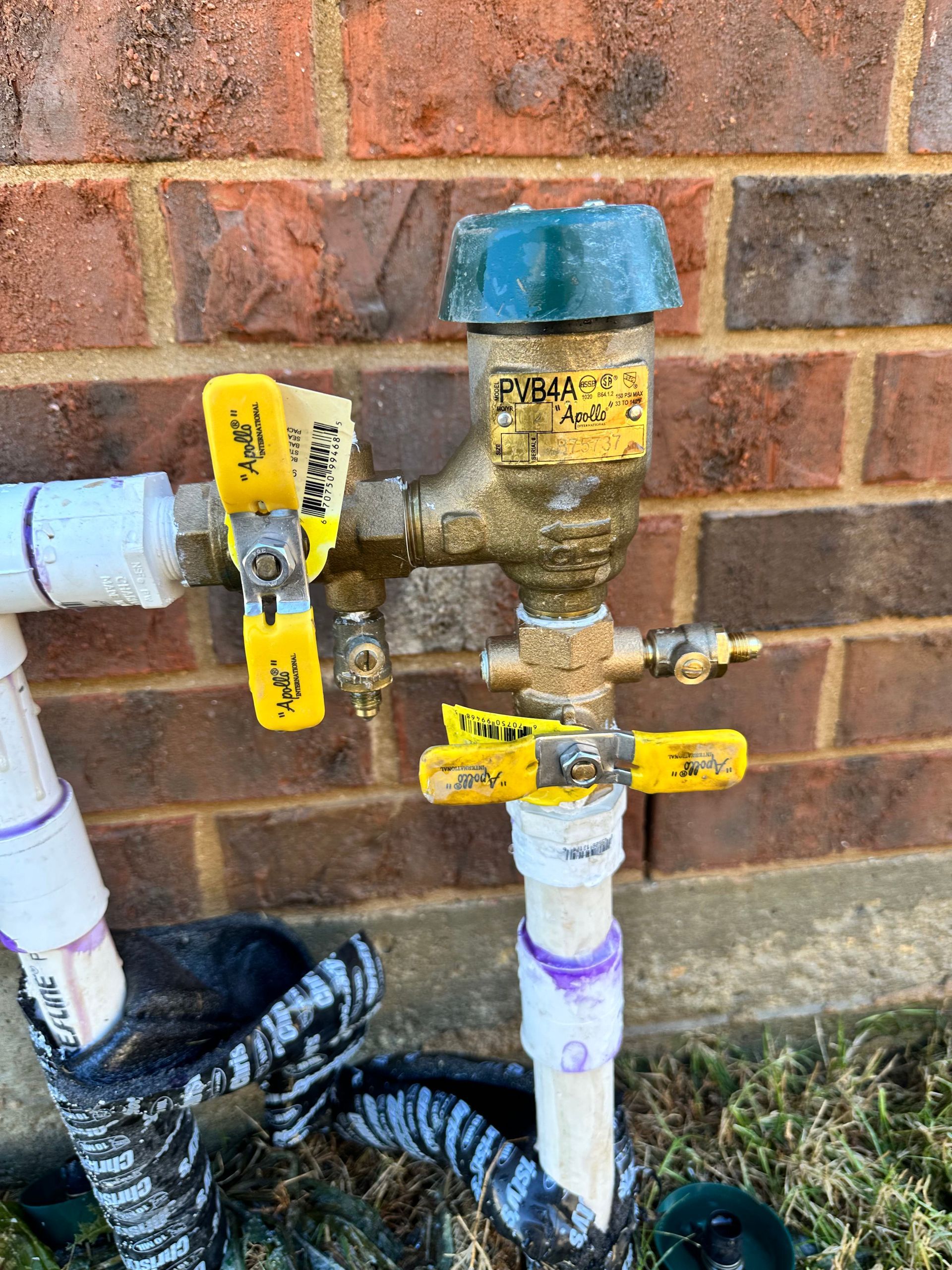 A hose with two yellow valves attached to it is sitting next to a brick wall.