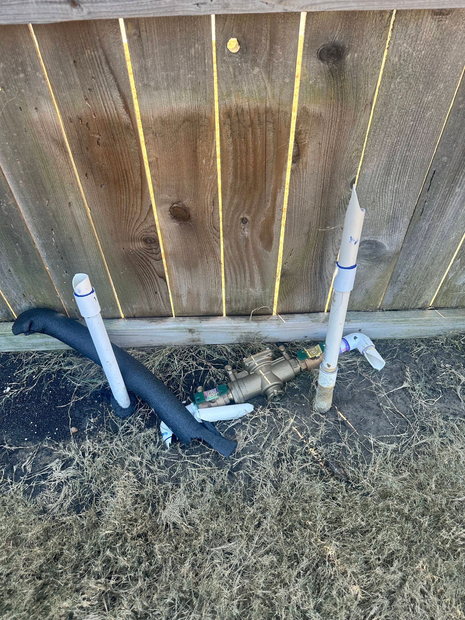 A hose is laying on the ground next to a wooden fence.