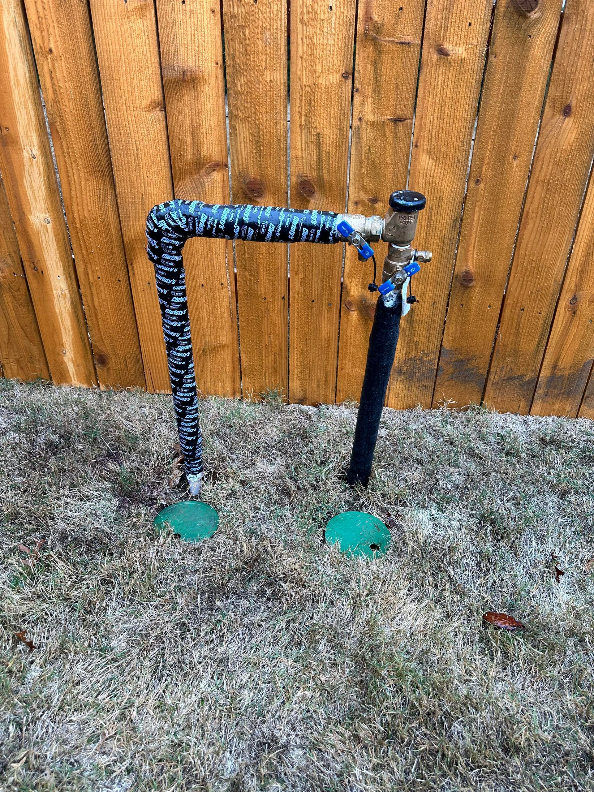 A sprinkler is sitting in the grass in front of a wooden fence.