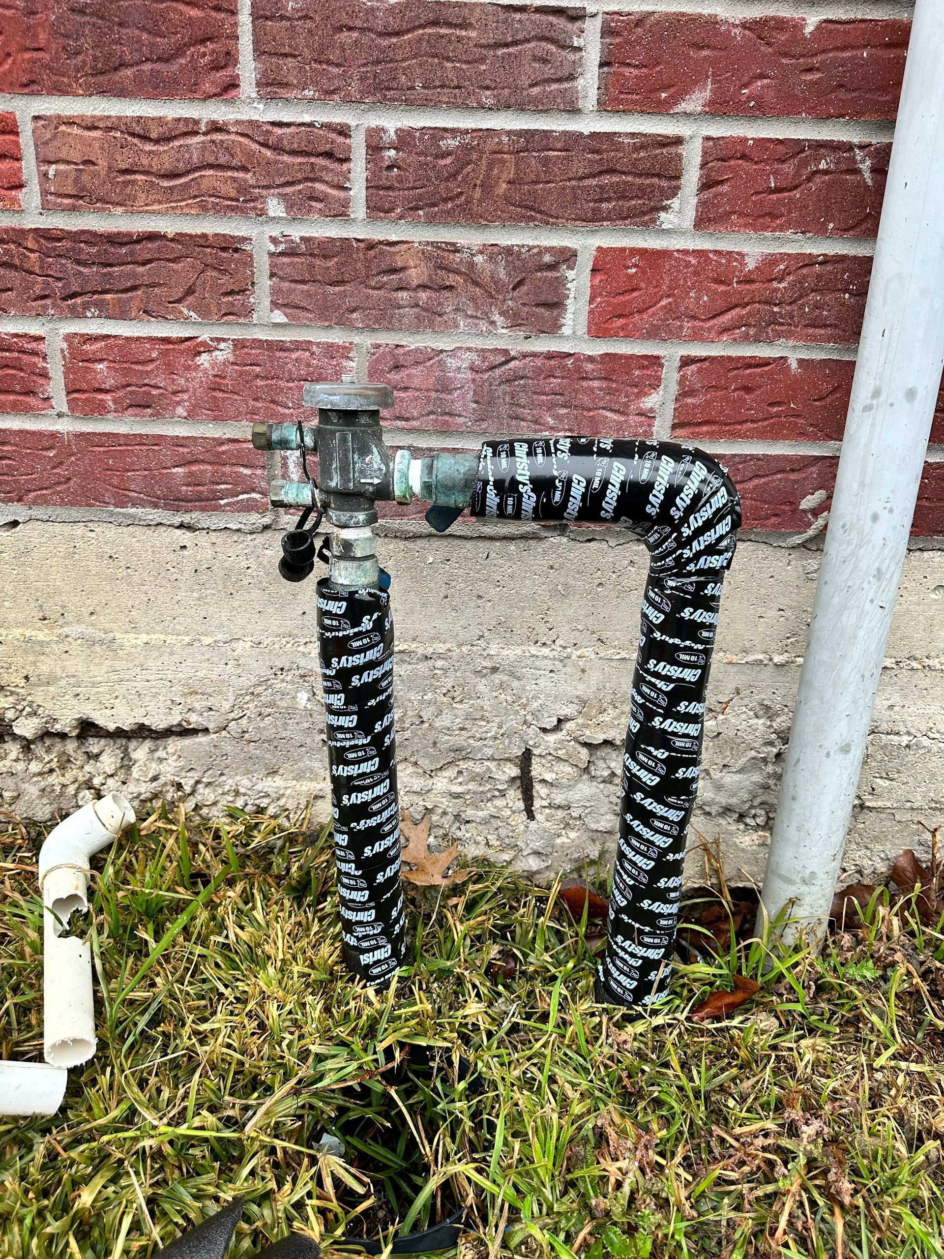 A hose is sitting in the grass next to a brick wall.