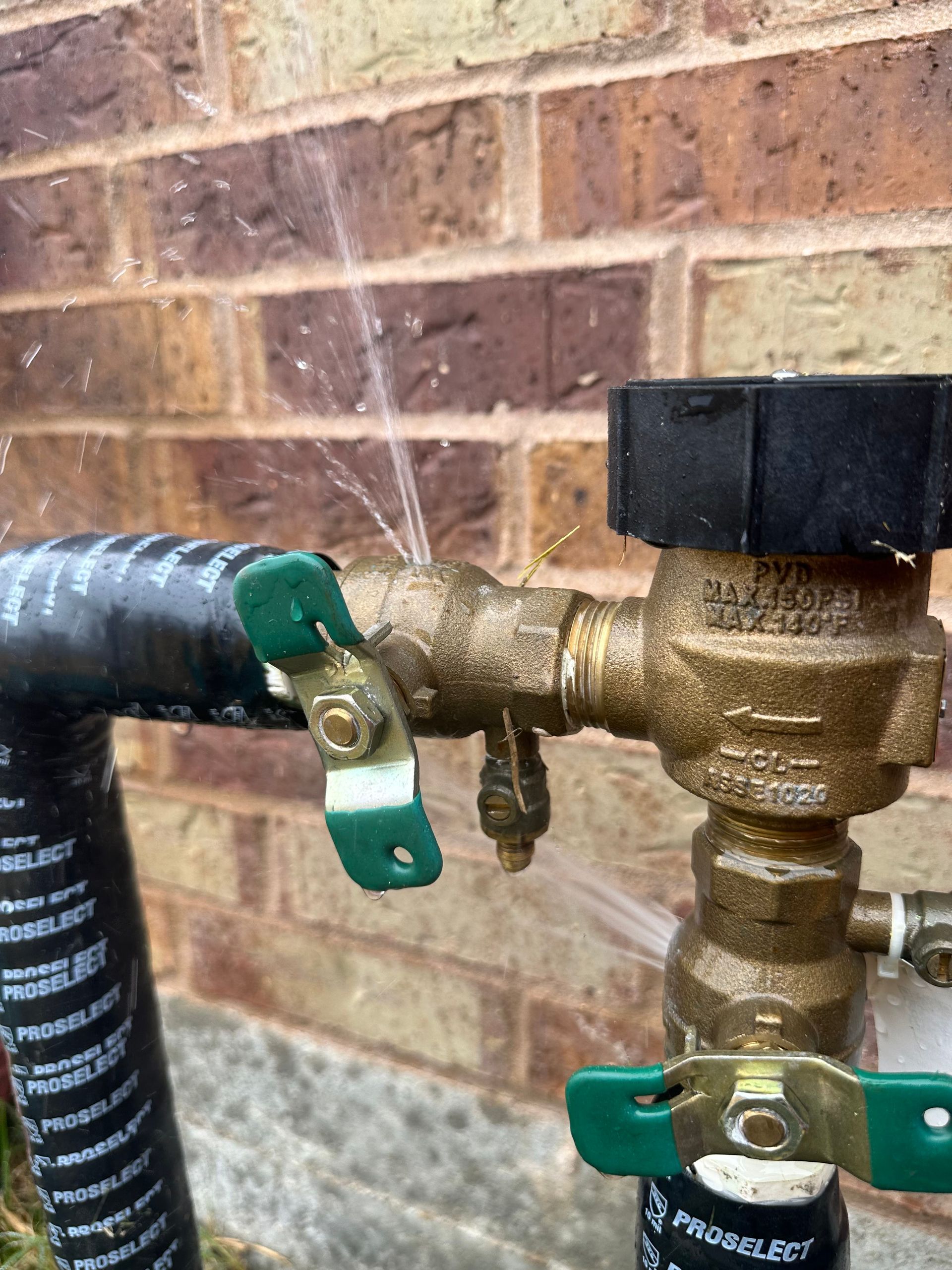 A close up of a faucet with water coming out of it against a brick wall.