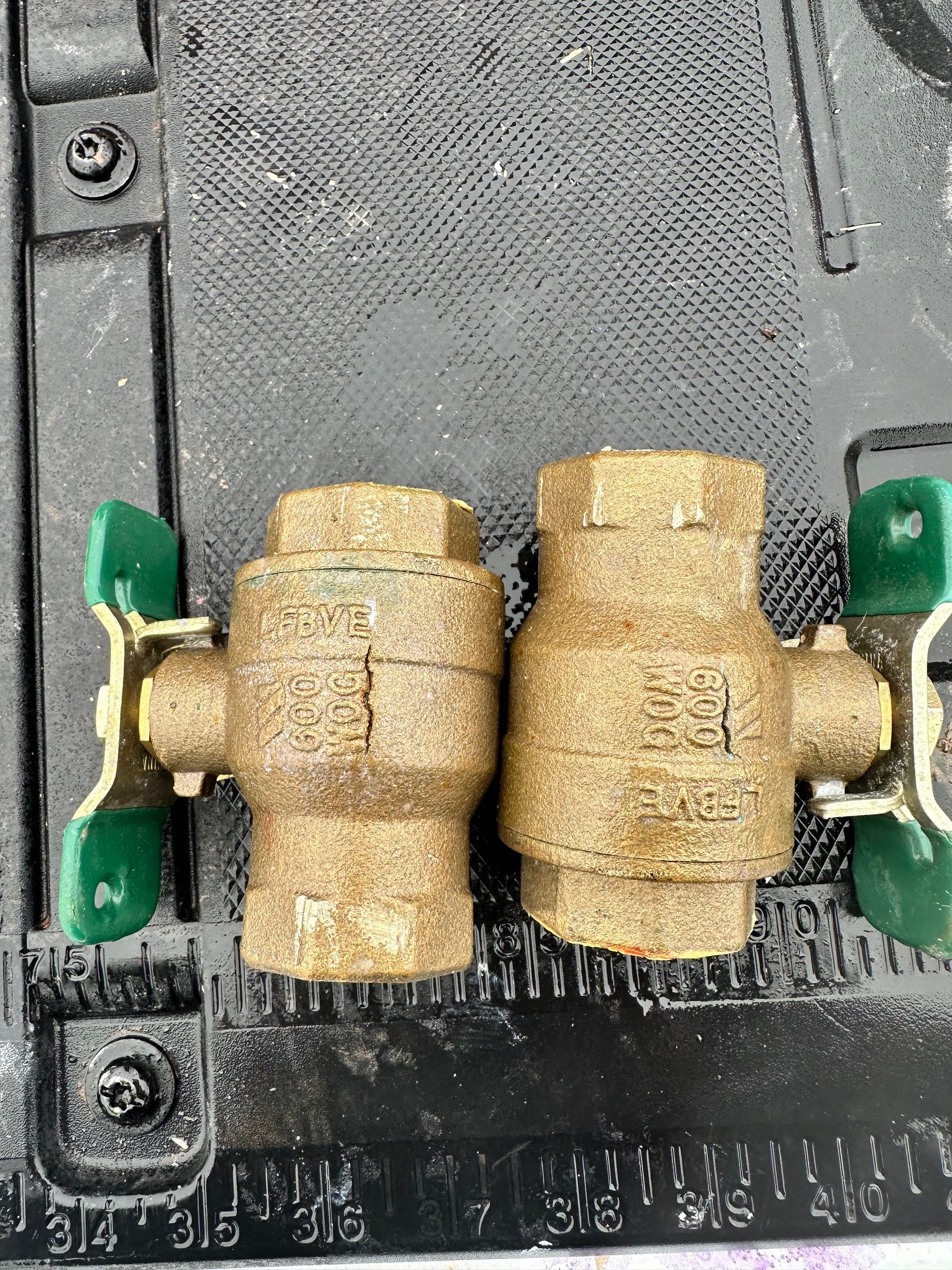 Two brass ball valves with green handles are sitting on top of a black surface.