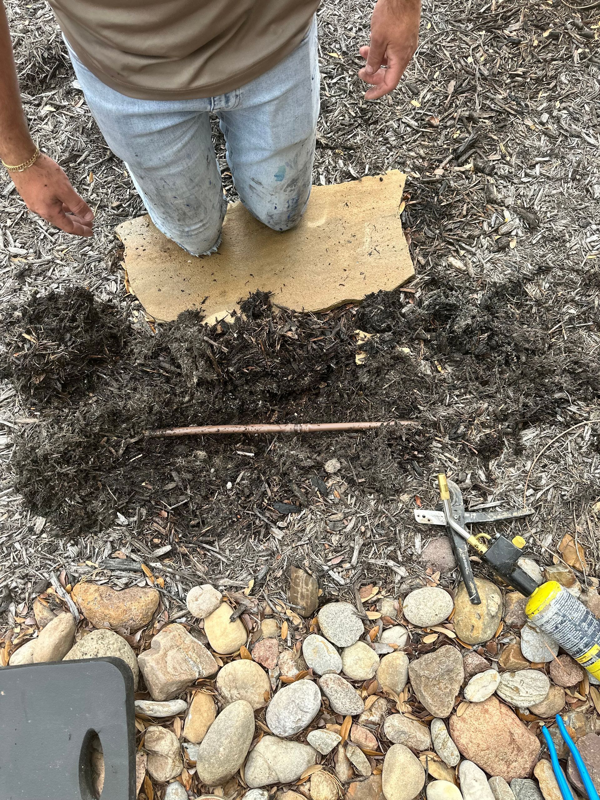 A person is kneeling on a piece of wood in the dirt.
