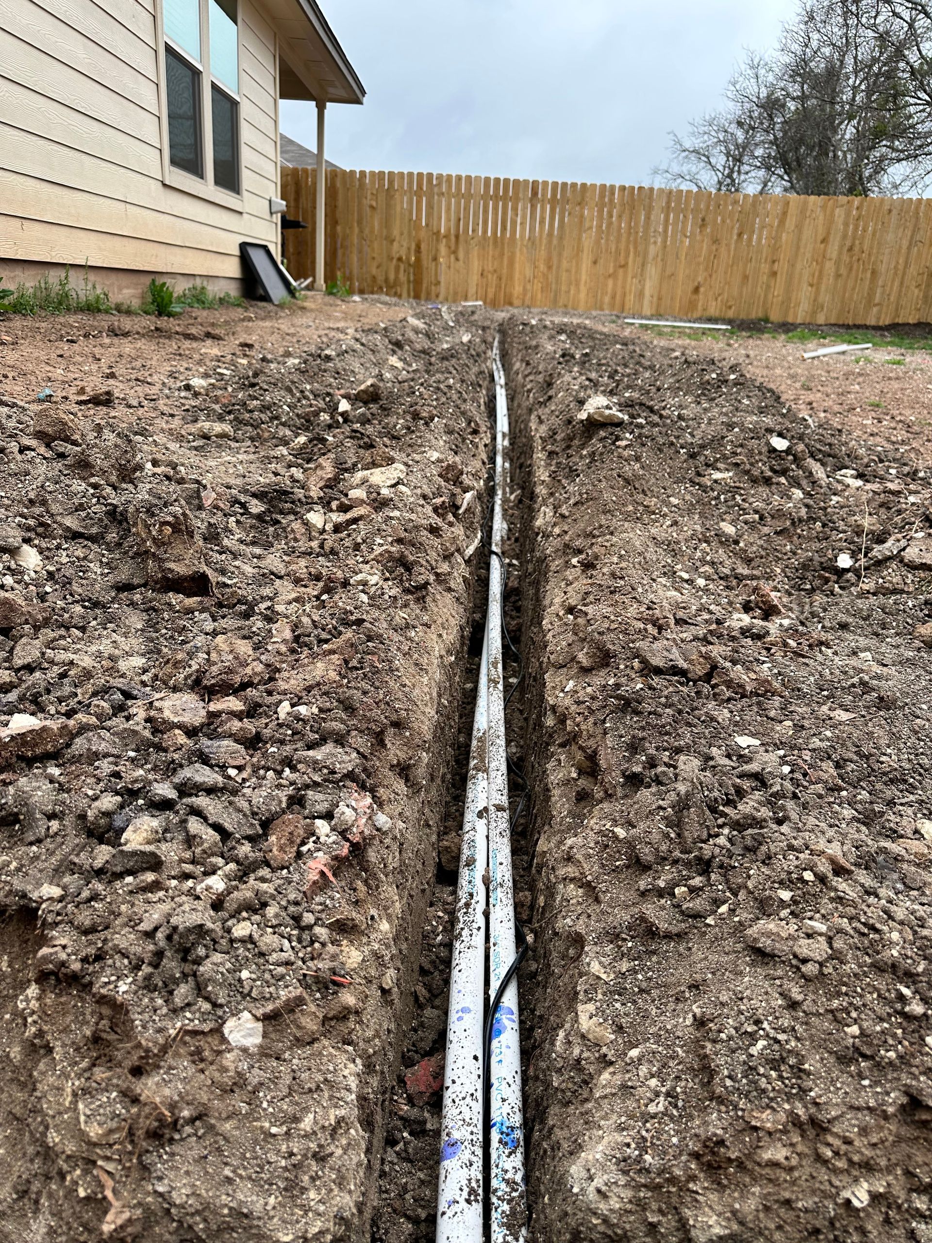 A drain pipe is being installed in the dirt in front of a house.
