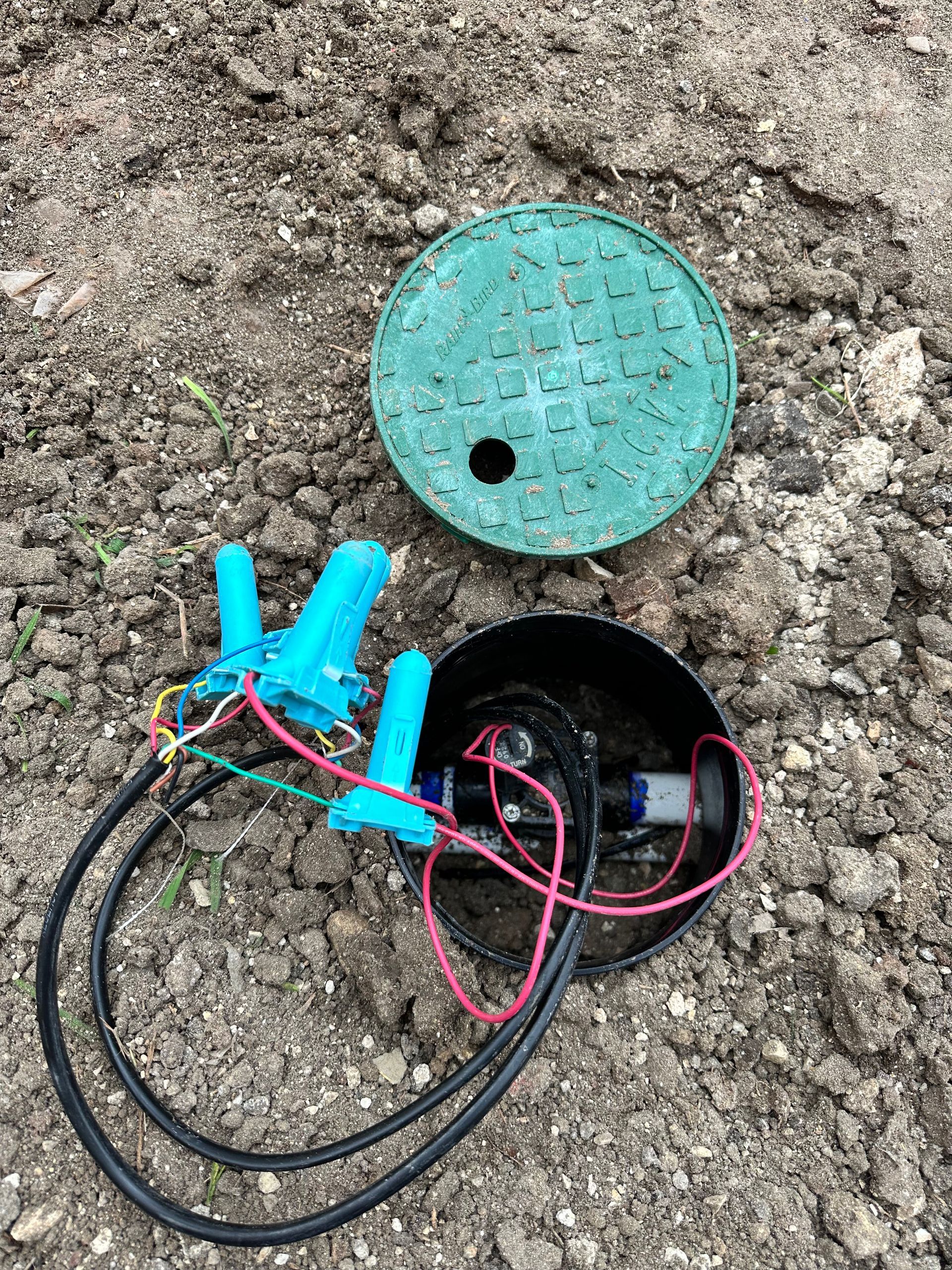 A sprinkler system is sitting in the dirt next to a green lid.