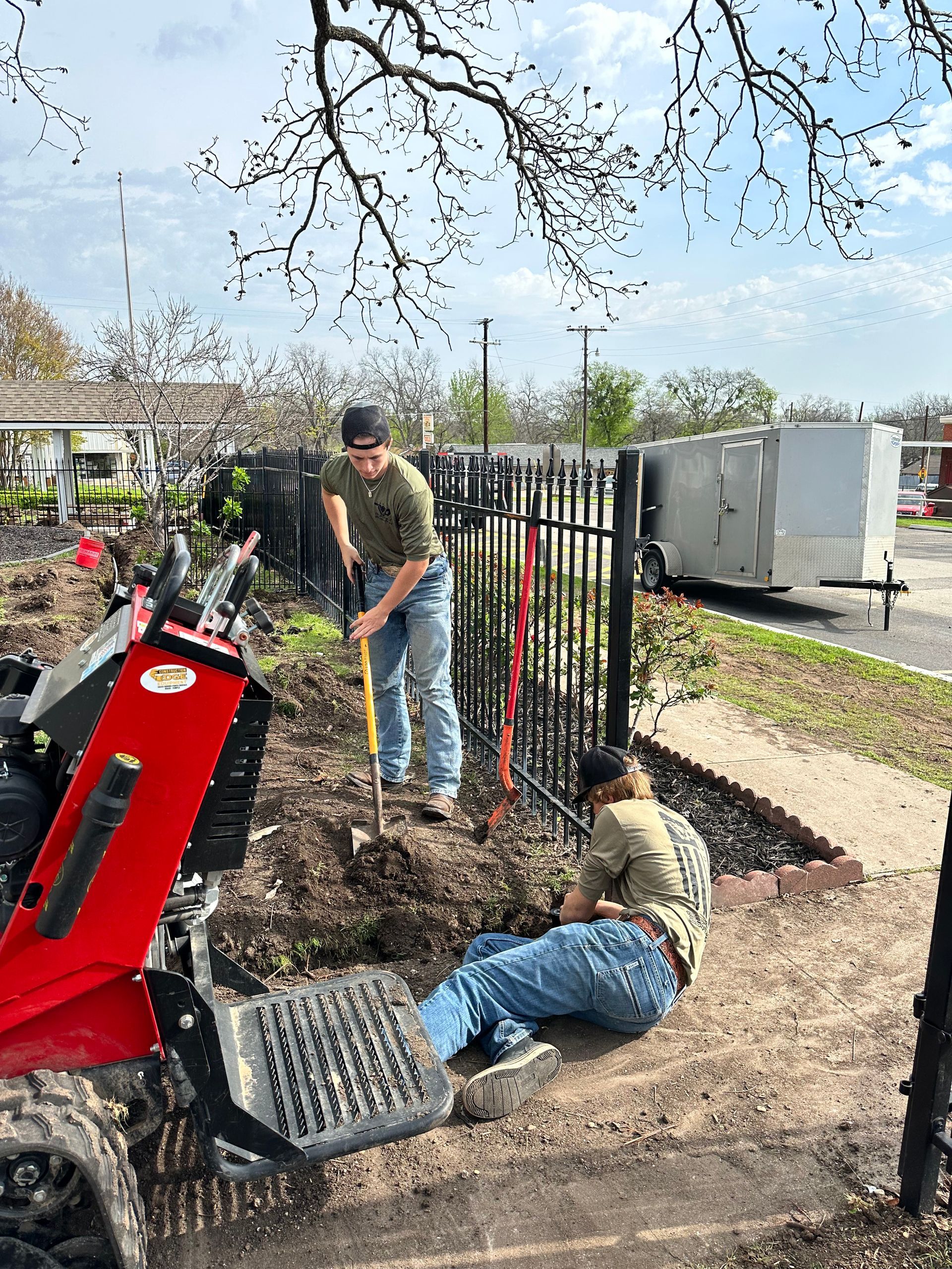 Two men are digging in the dirt next to a tractor.
