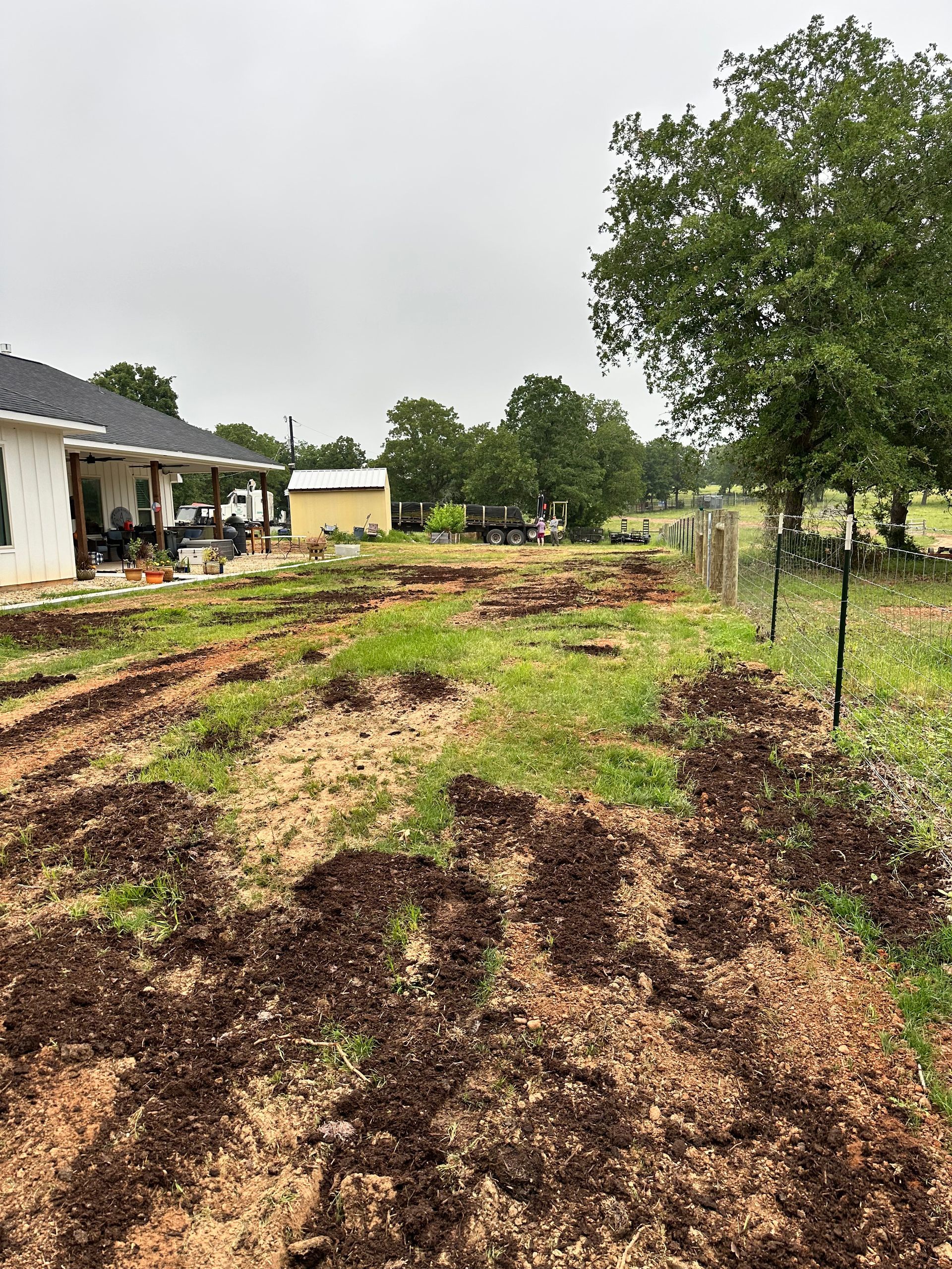 A muddy field with a house in the background and a fence in the foreground.