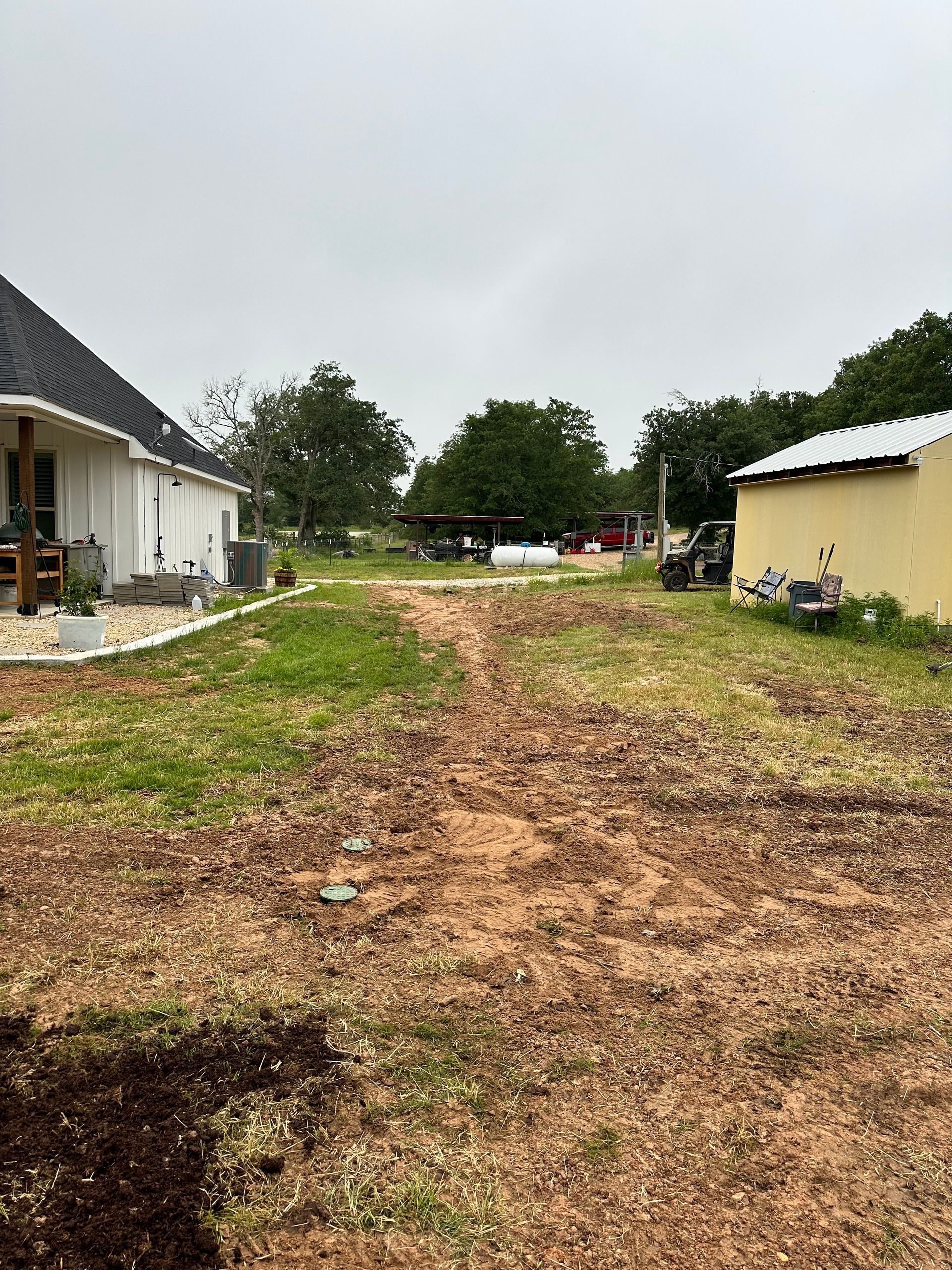 A dirt road leading to a house in the middle of a grassy field.