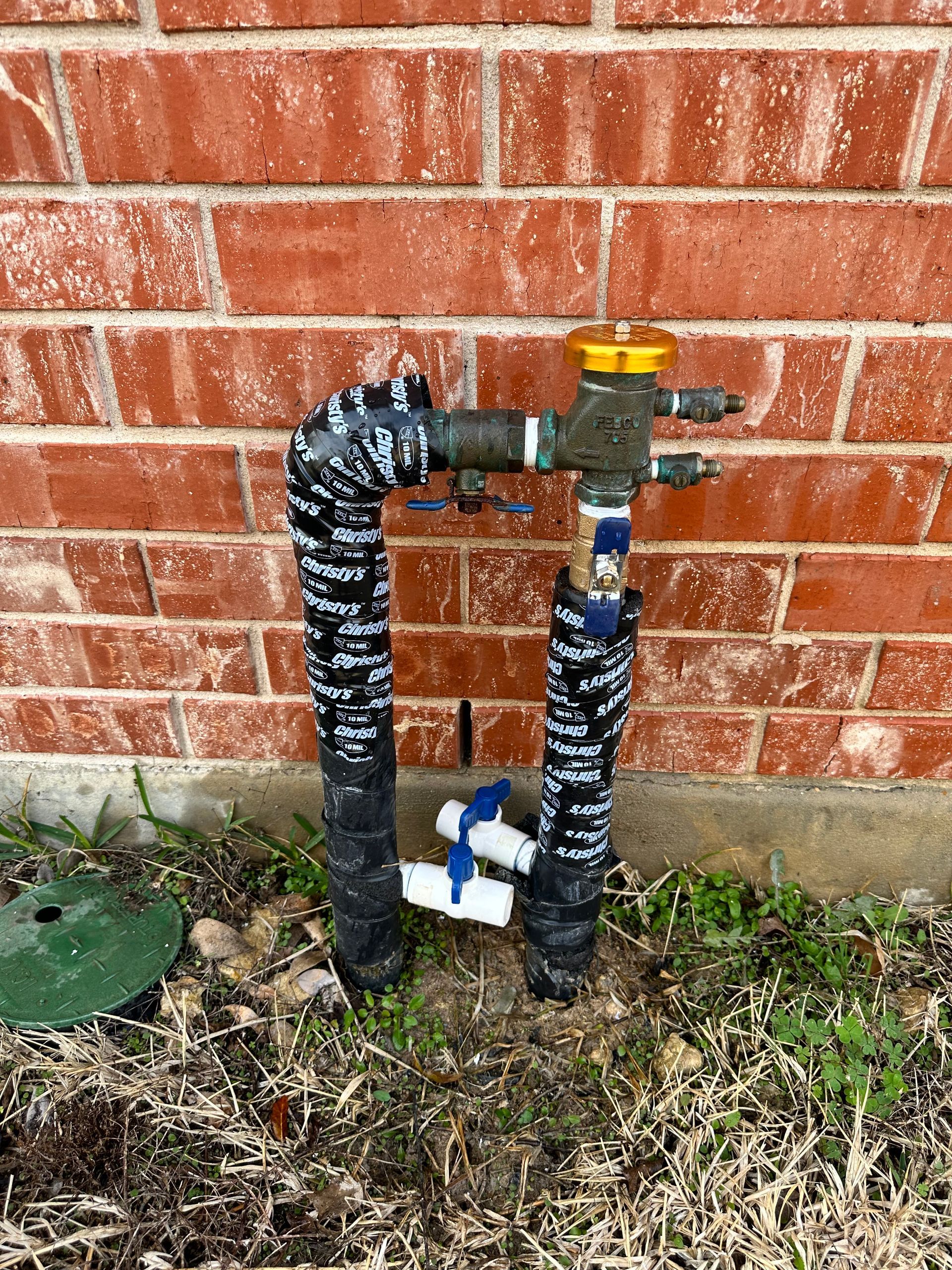 A hose with a valve attached to it is sitting in front of a brick wall.