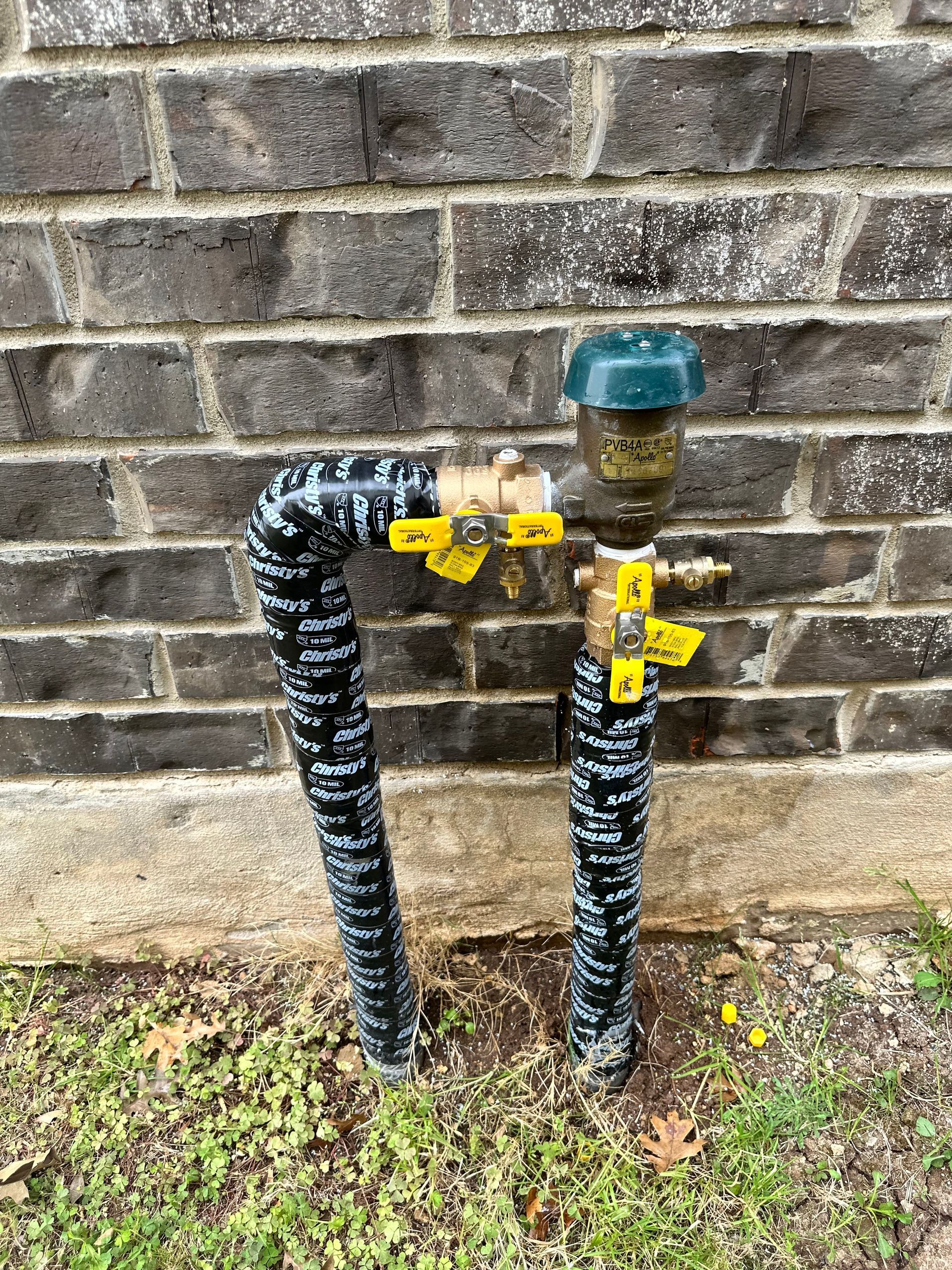 A hose is attached to a faucet on the side of a brick wall.