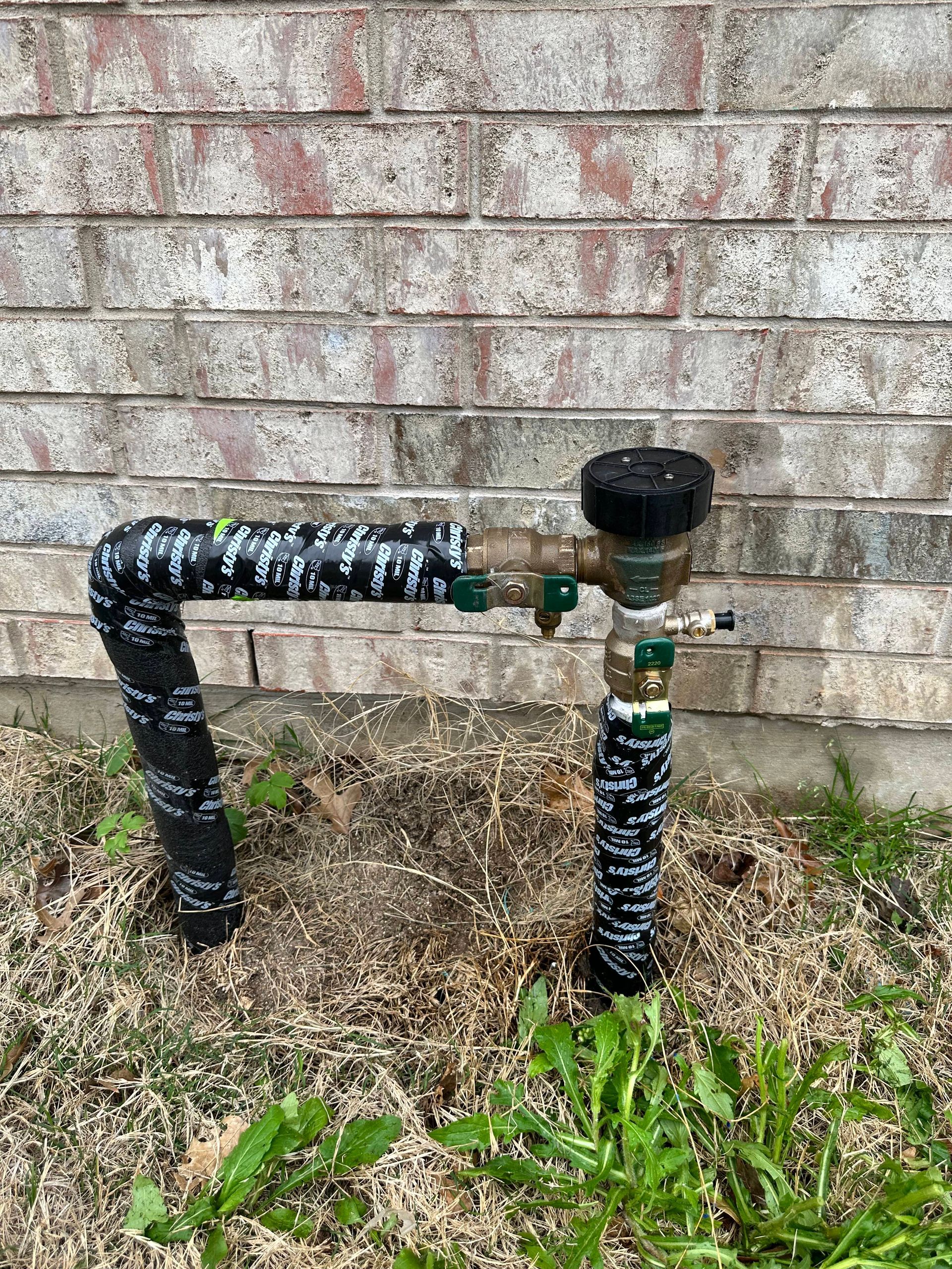 A hose is sitting in the grass next to a brick wall.