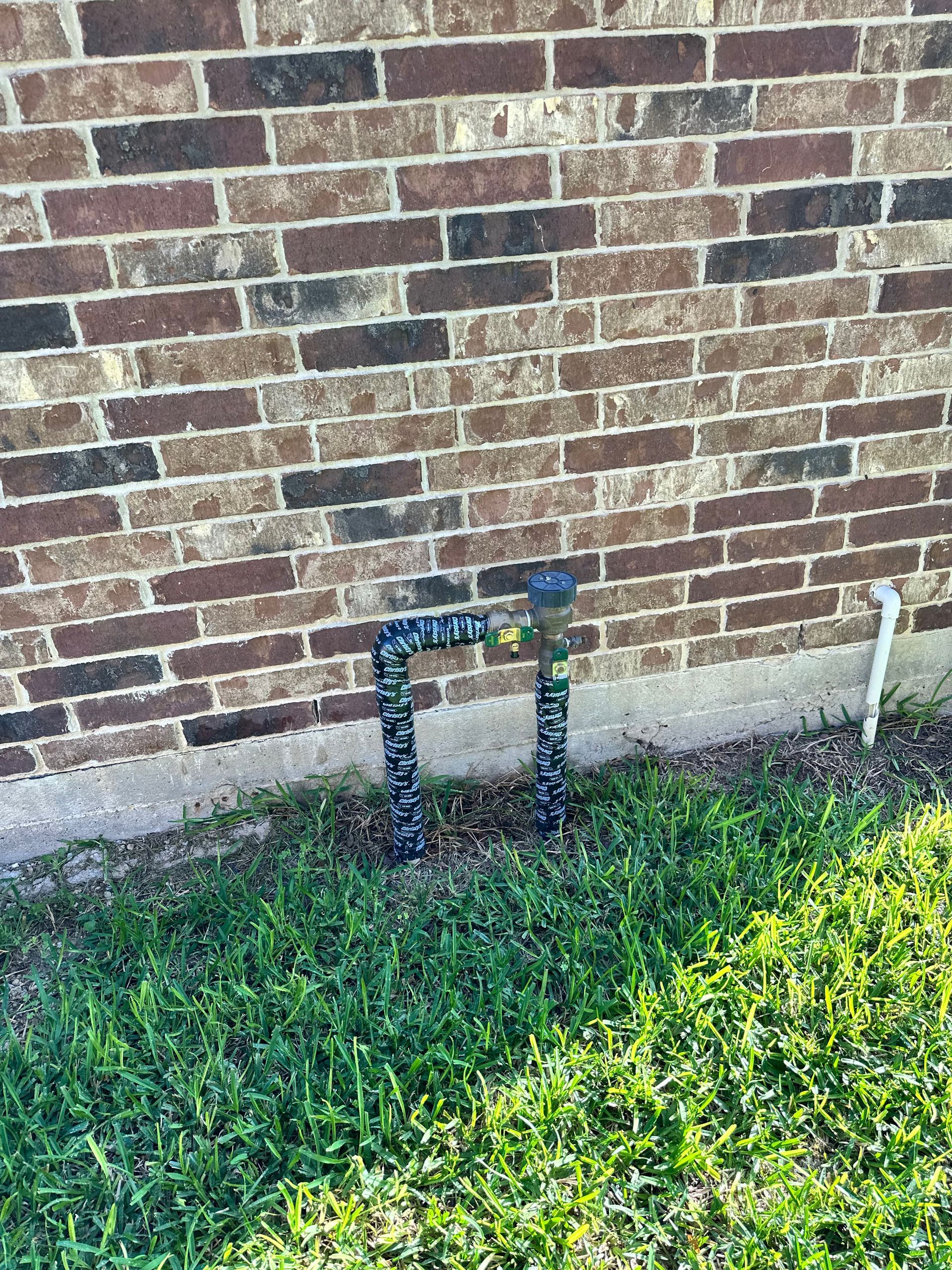 A hose is sitting in the grass next to a brick wall.