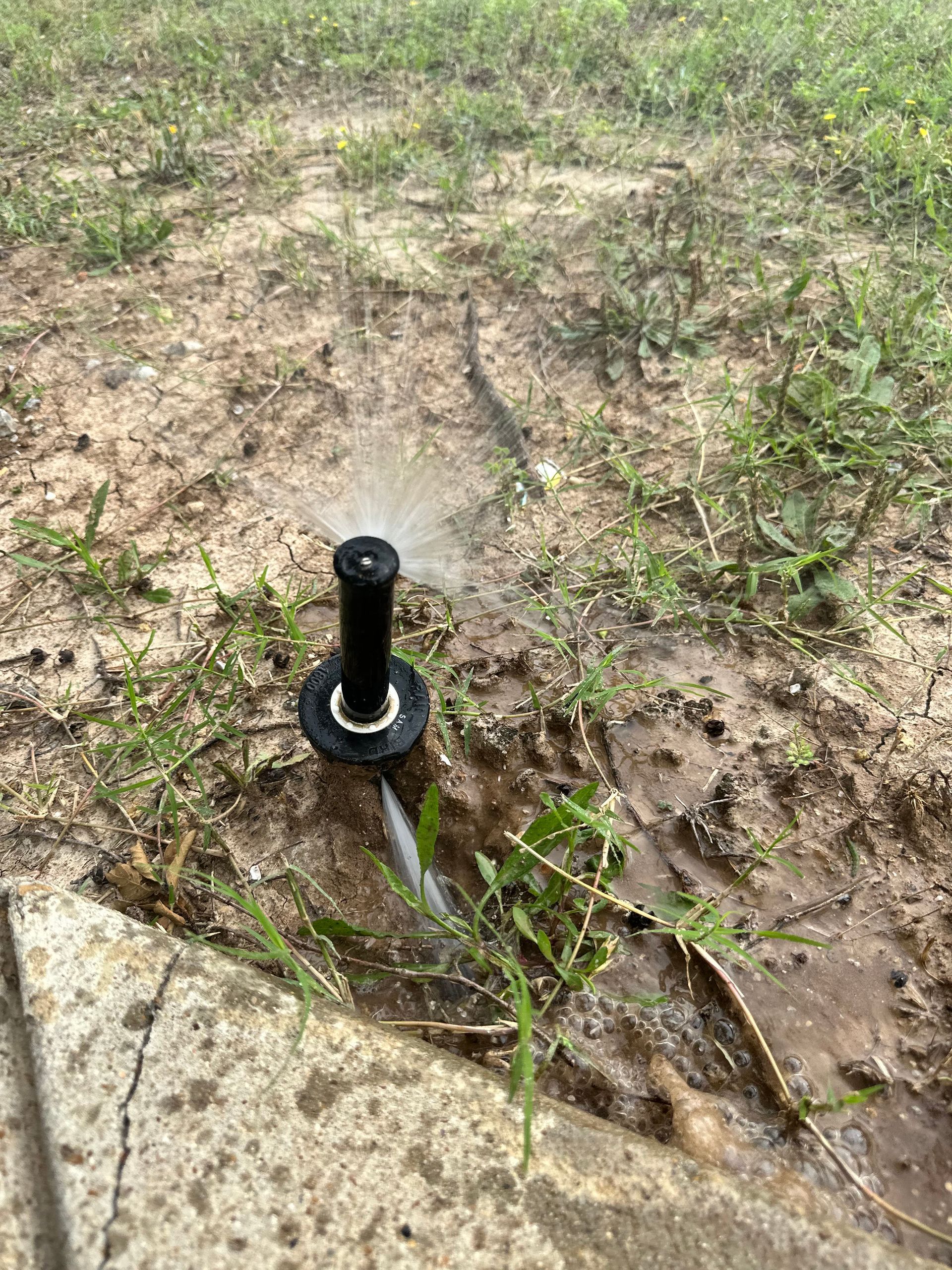 A sprinkler is spraying water in a muddy field.