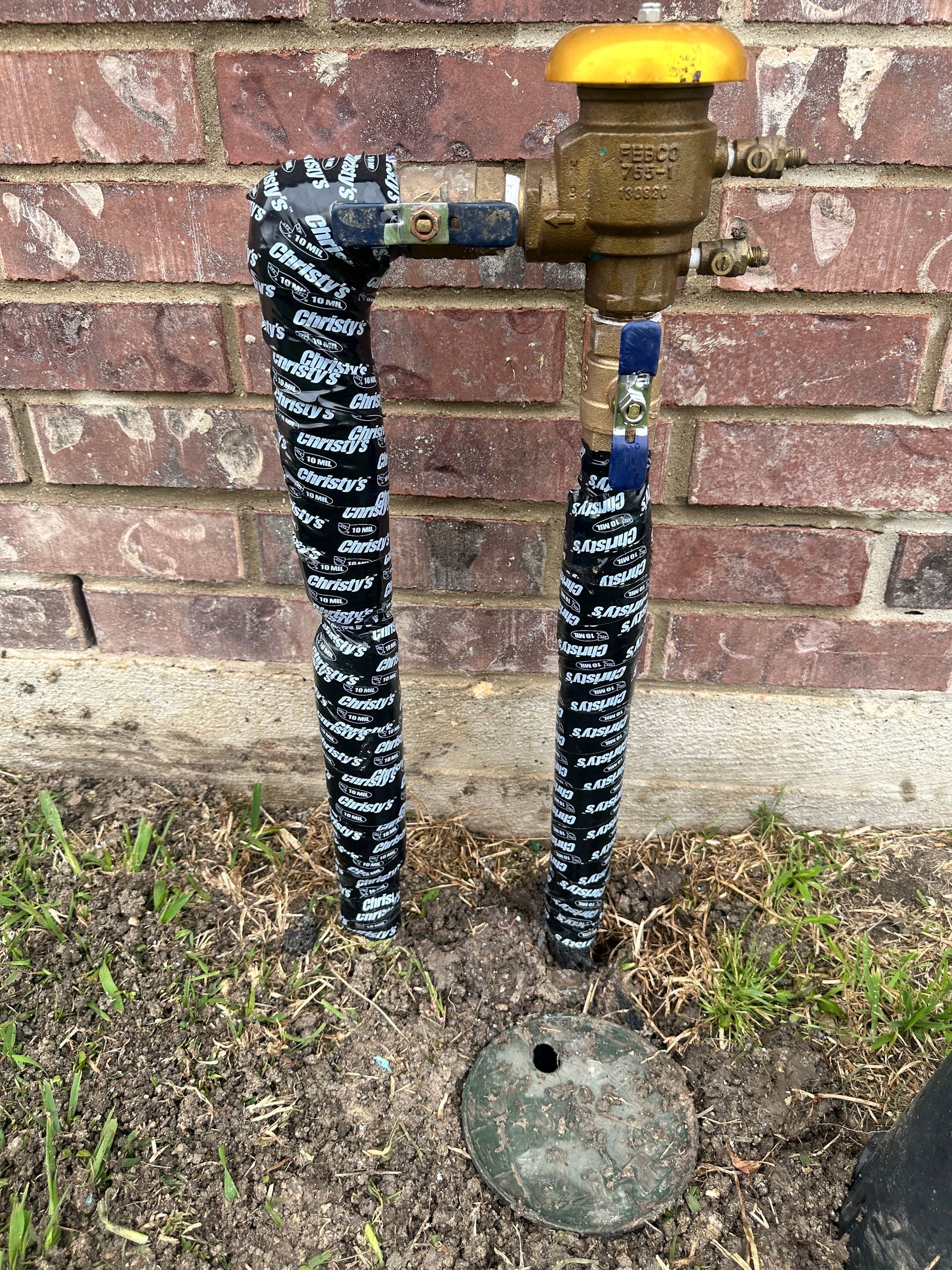 A hose with a yellow cap is sitting next to a brick wall.