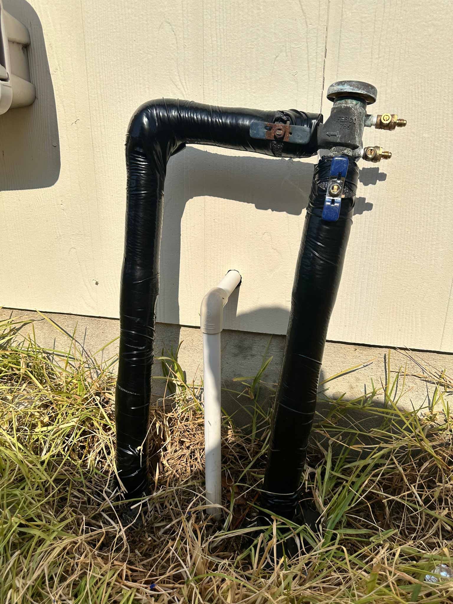 A black pipe is sitting in the grass next to a wall.