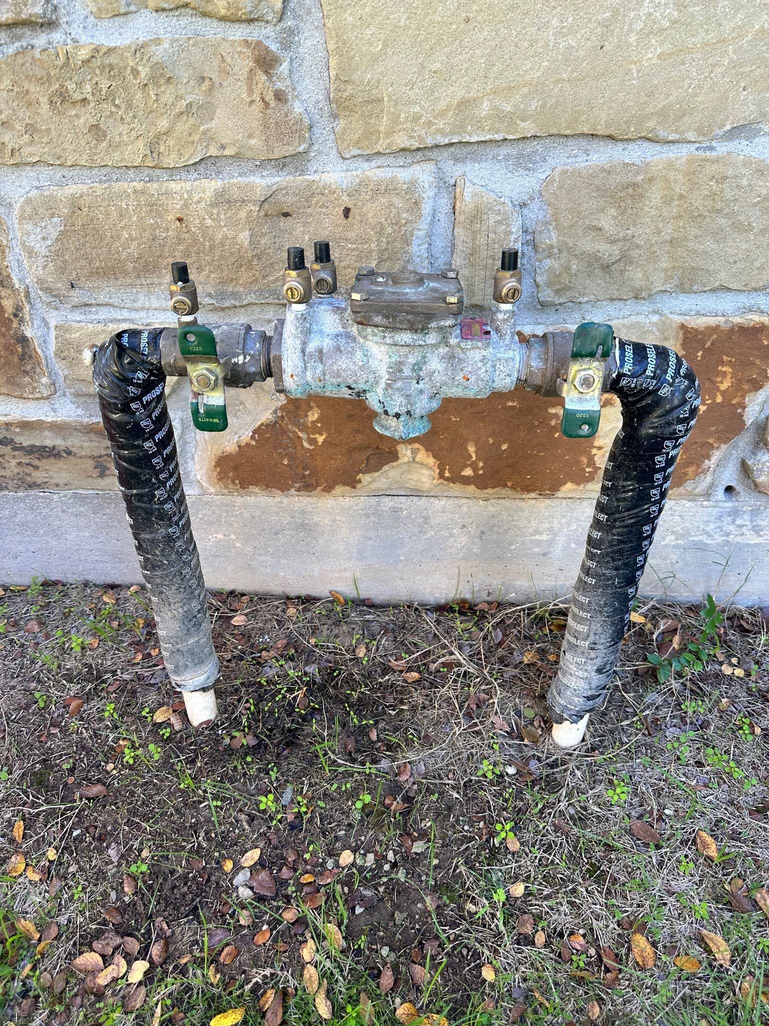 A water meter is sitting on the ground next to a brick wall.