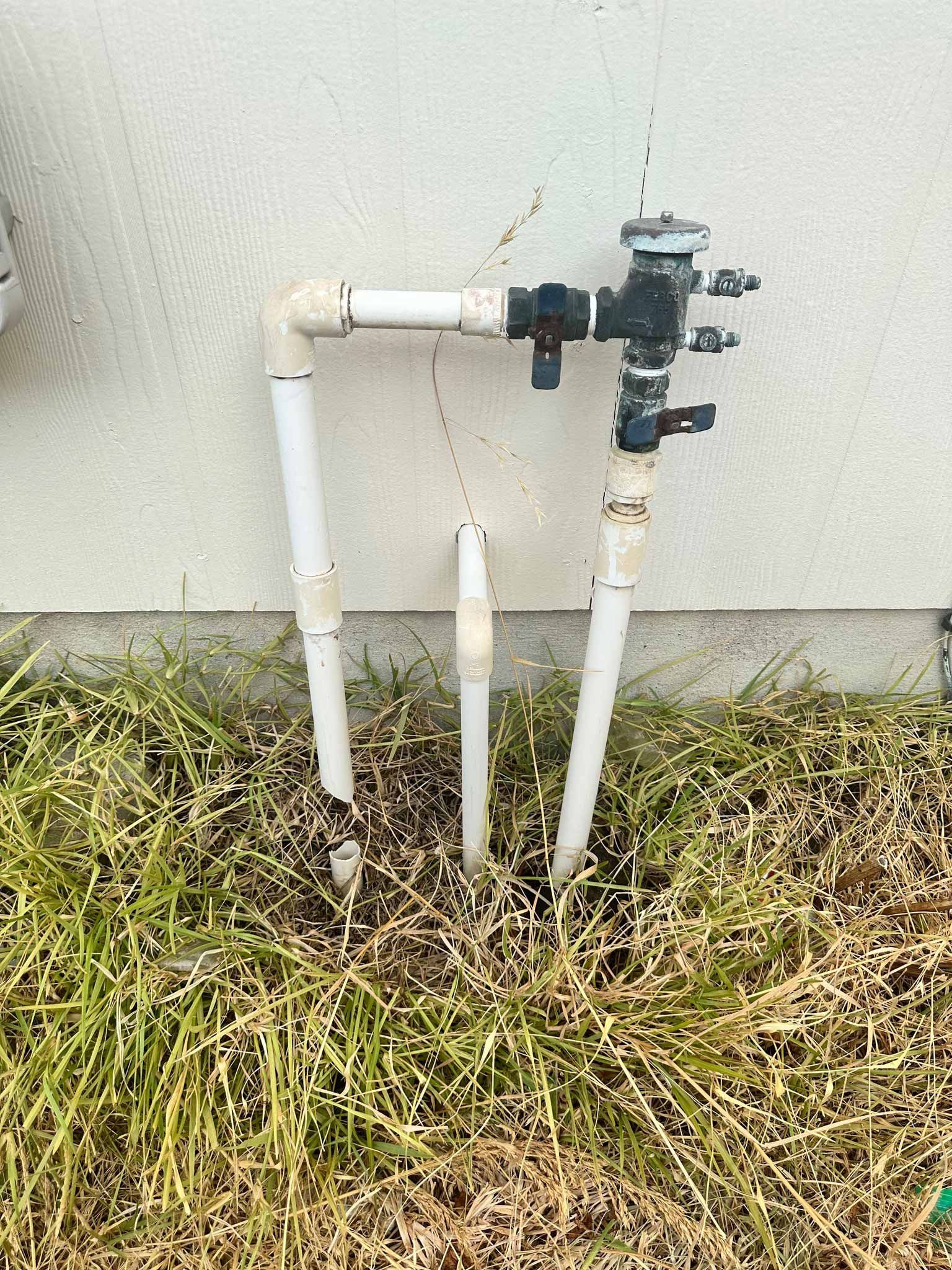 A water pipe is sitting in the grass next to a wall.