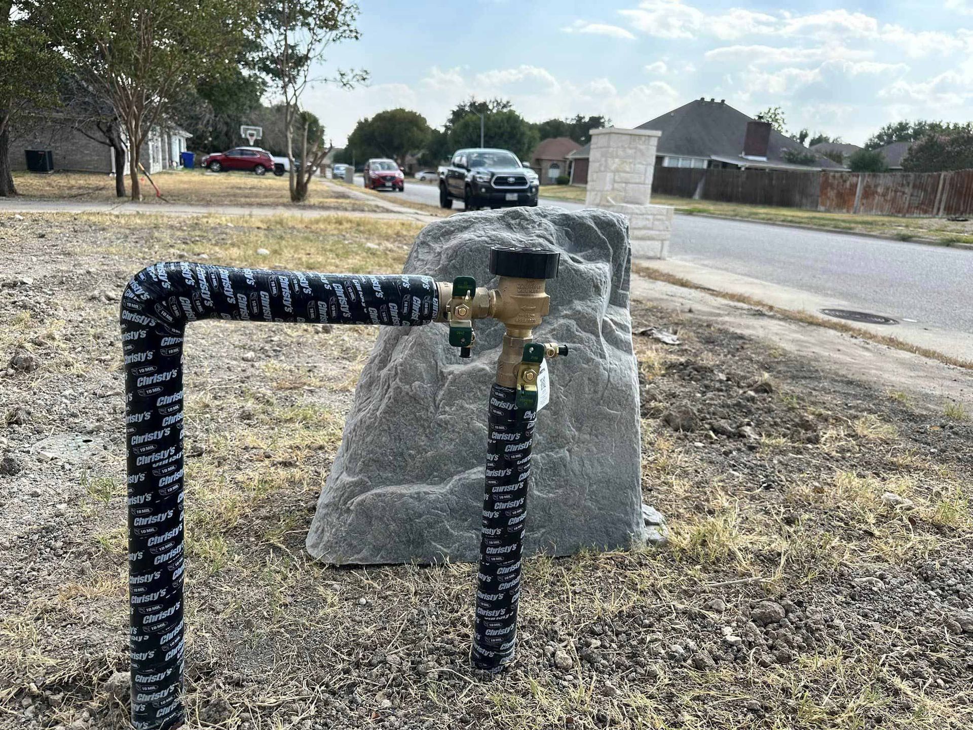 A hose is attached to a rock in the grass next to a street.