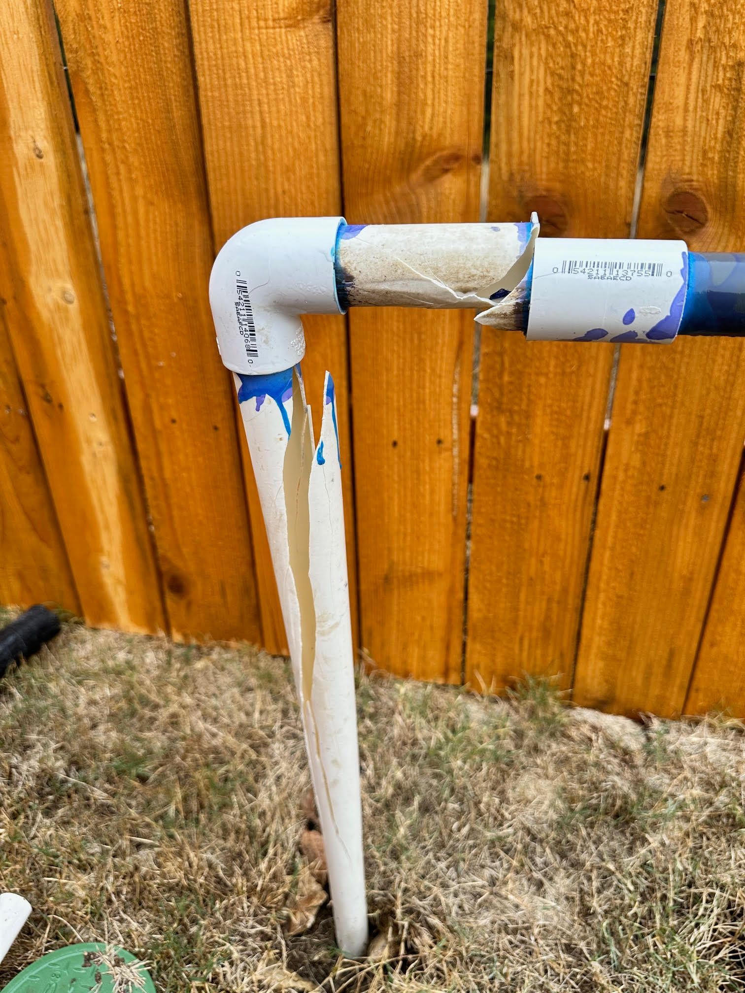 A white pipe is sitting in the dirt in front of a wooden fence.