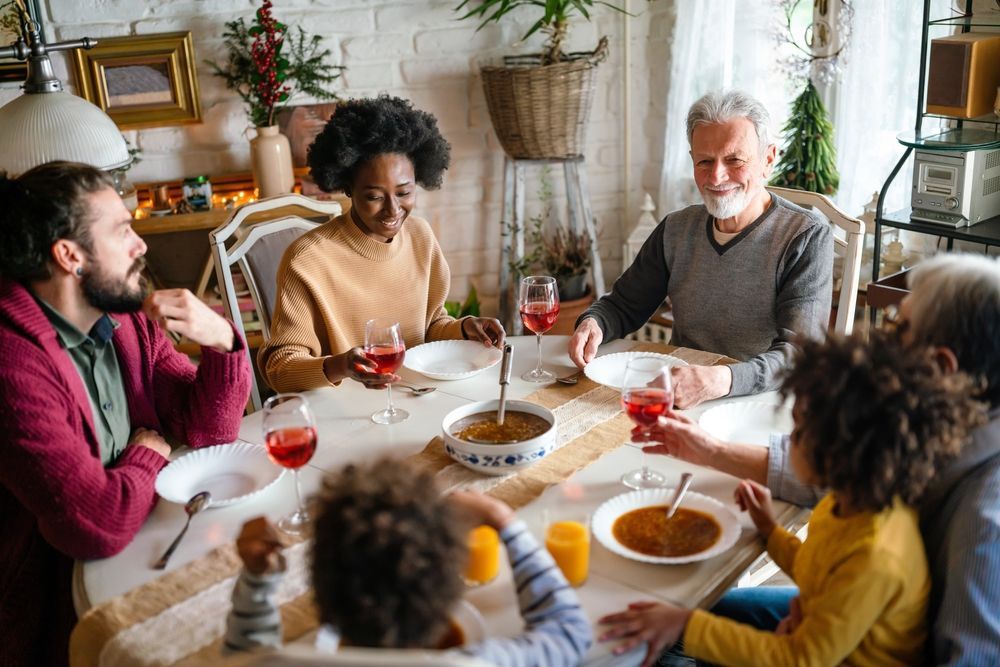 Family gathered around a table, smiling and eating; two children, adults of different ages, drinking, and sharing a meal.