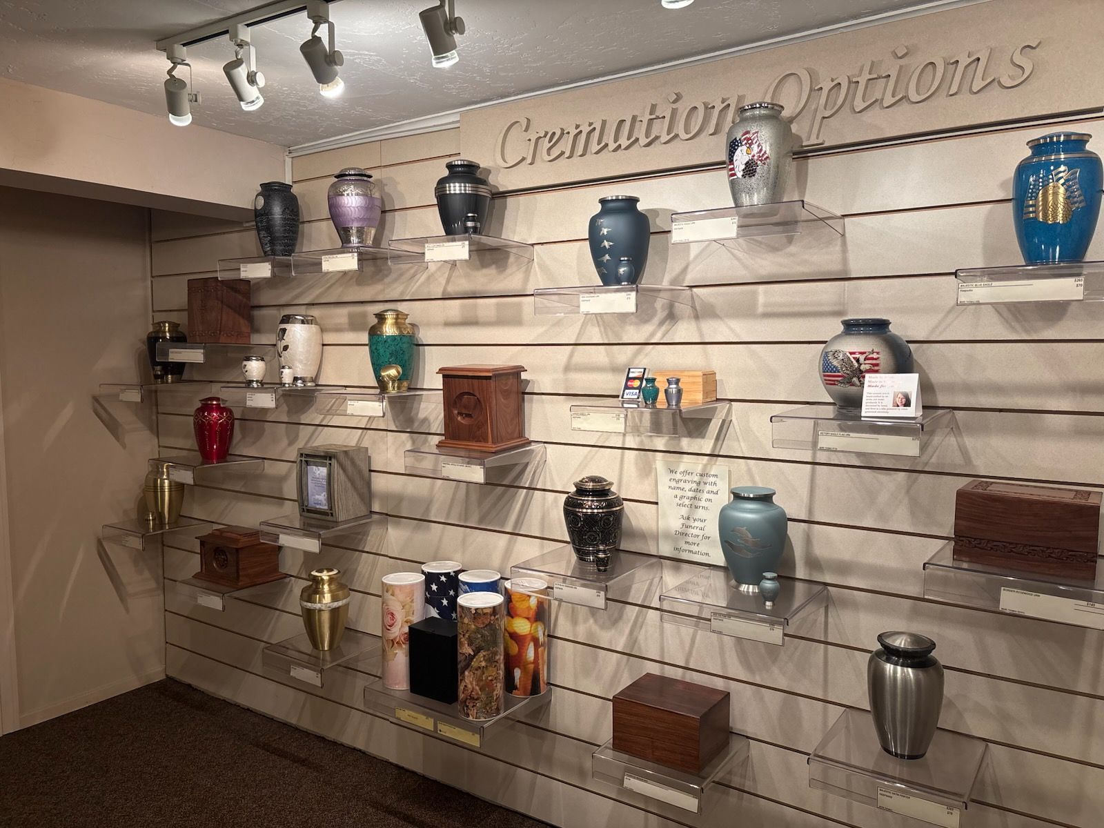 A display of cremation urns of various shapes, sizes, and colors on shelves labeled 
