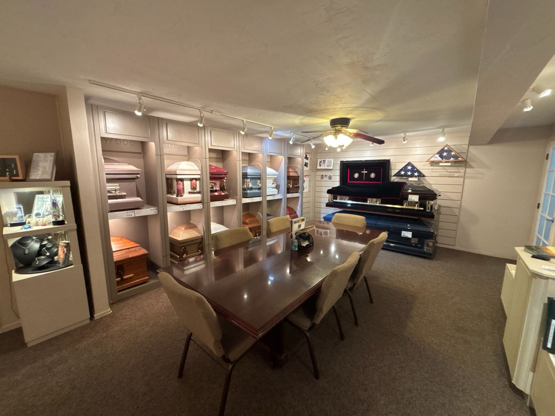 Funeral home showroom with caskets displayed. A long table with chairs is in the center.