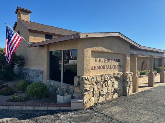 H.K. Holland Memorial Chapel, beige stucco building with American flag, blue sky.