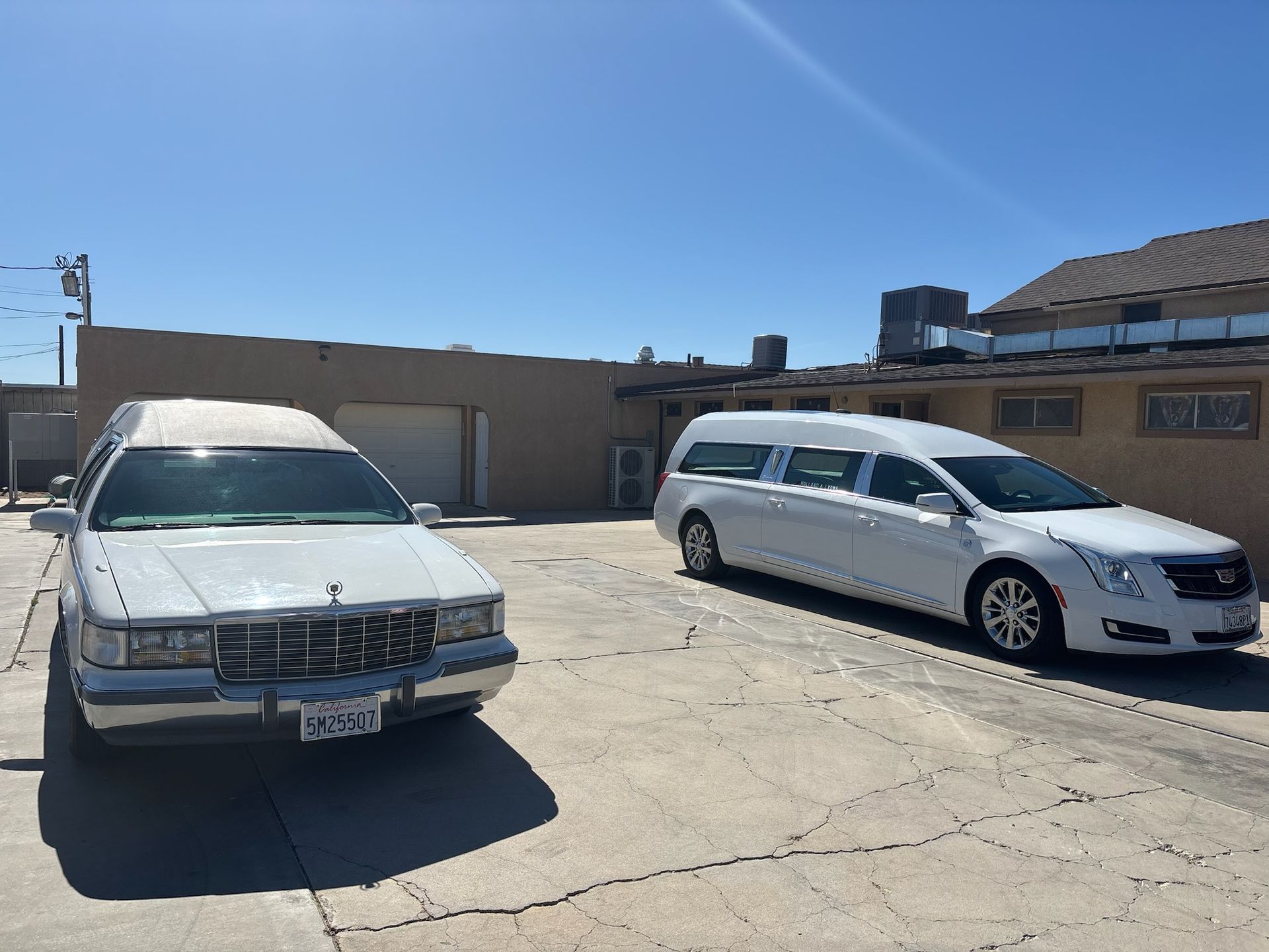 Two white hearses parked in a paved lot on a sunny day.