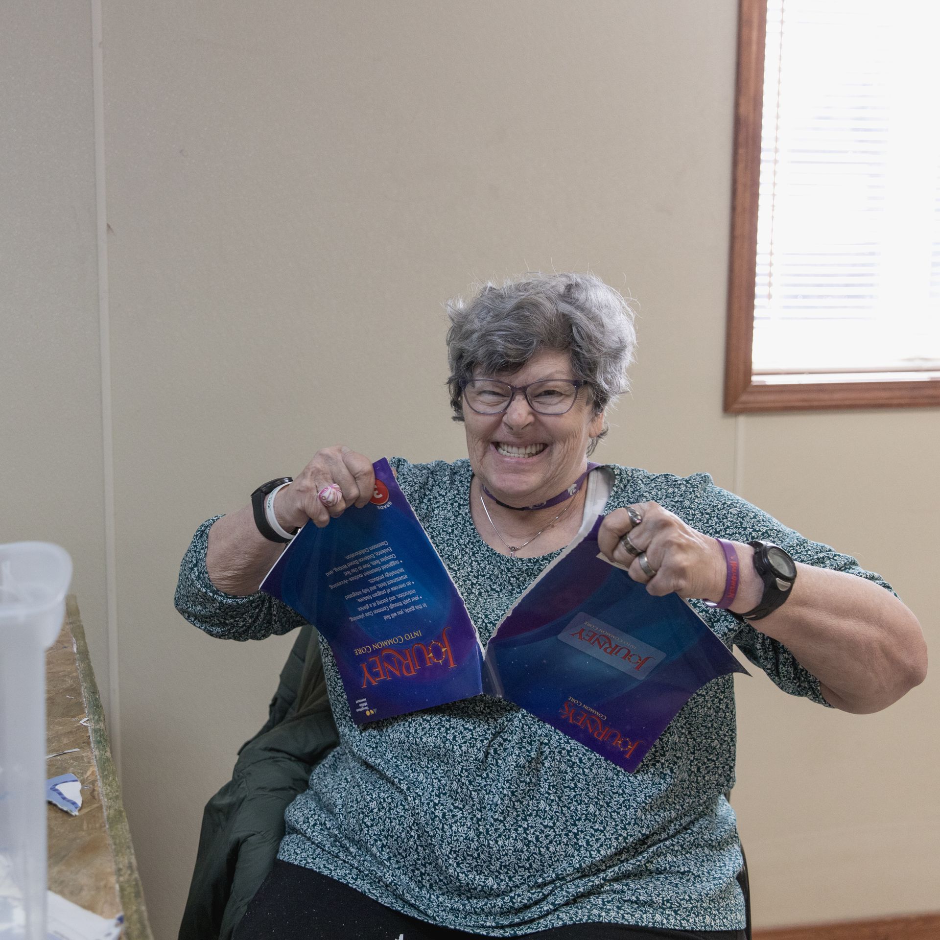 A woman in a green shirt is holding two books in her hands and smiling