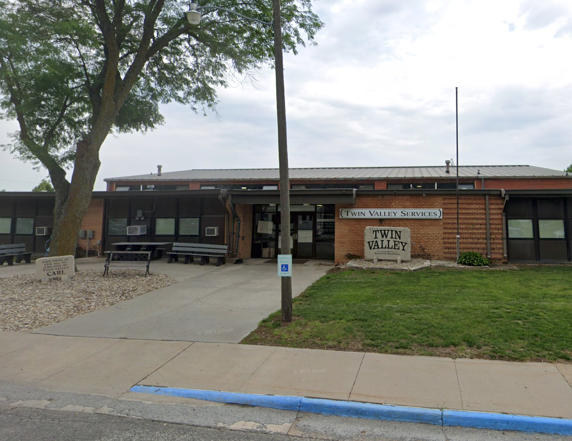A school building with a blue curb and a tree in front of it.