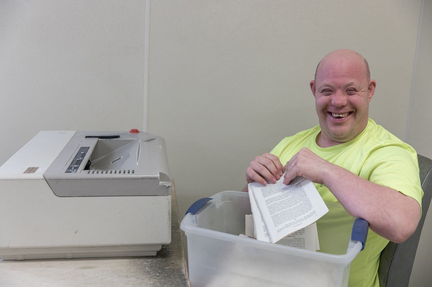 A man is sitting in front of a printer holding a piece of paper.