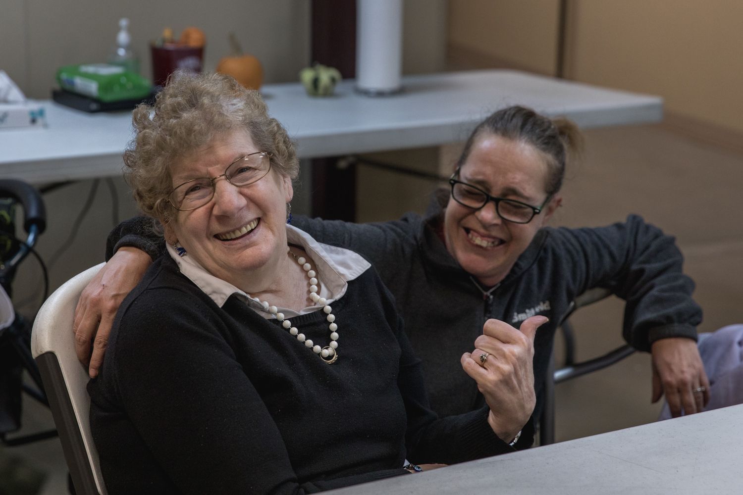 Two women are sitting at a table with their arms around each other.