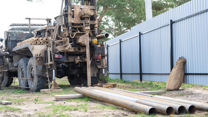 A truck is drilling a hole in the ground next to a pile of pipes.