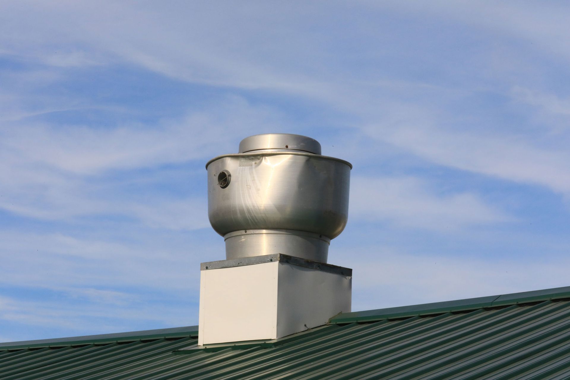 A chimney on top of a green roof with a blue sky in the background.