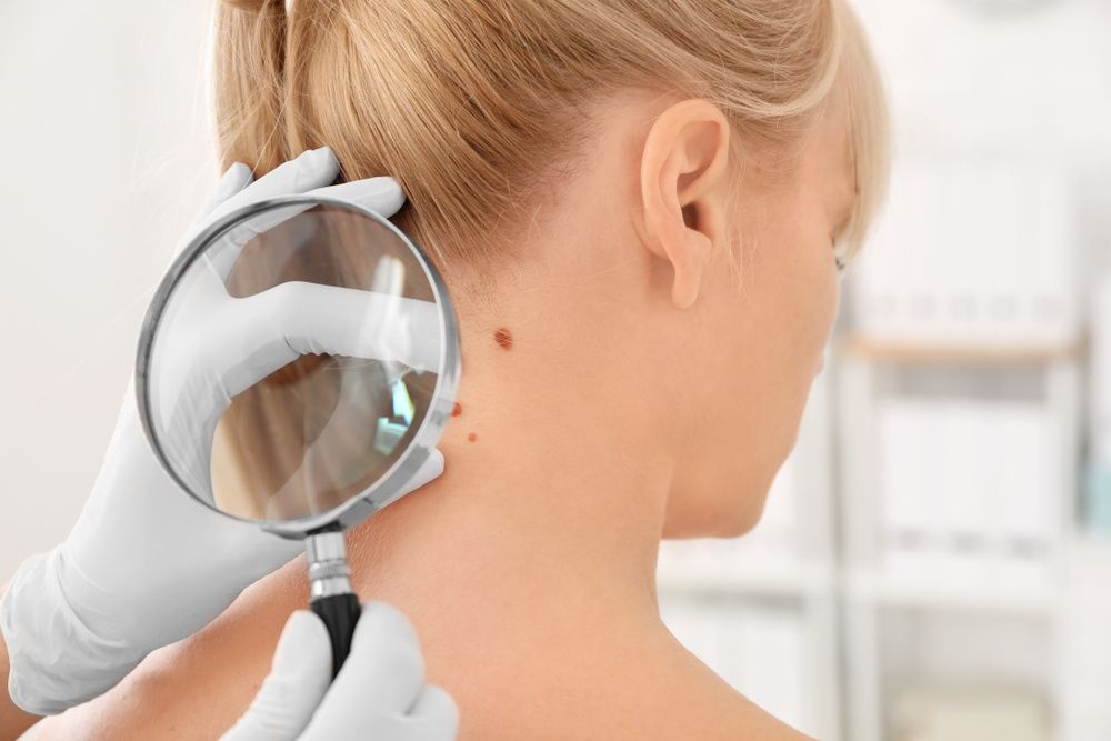 A Doctor is Examining a Woman Neck With a Magnifying Glass — Coastal Skin & Laser in Mooloolaba, QLD