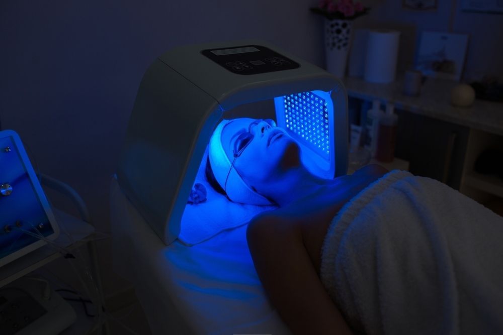A Woman is Laying on a Bed With a Blue Light on Her Face — Coastal Skin & Laser in Mooloolaba, QLD