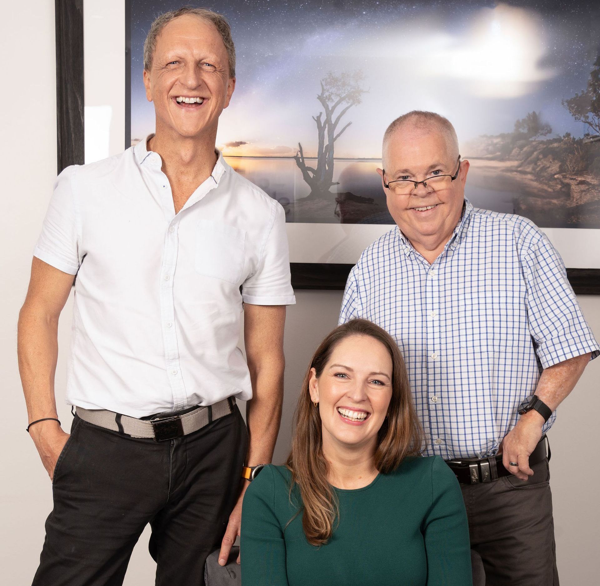 A Woman in green on a chair and two men standing behind her — Coastal Skin & Laser in Tewantin, QLD 